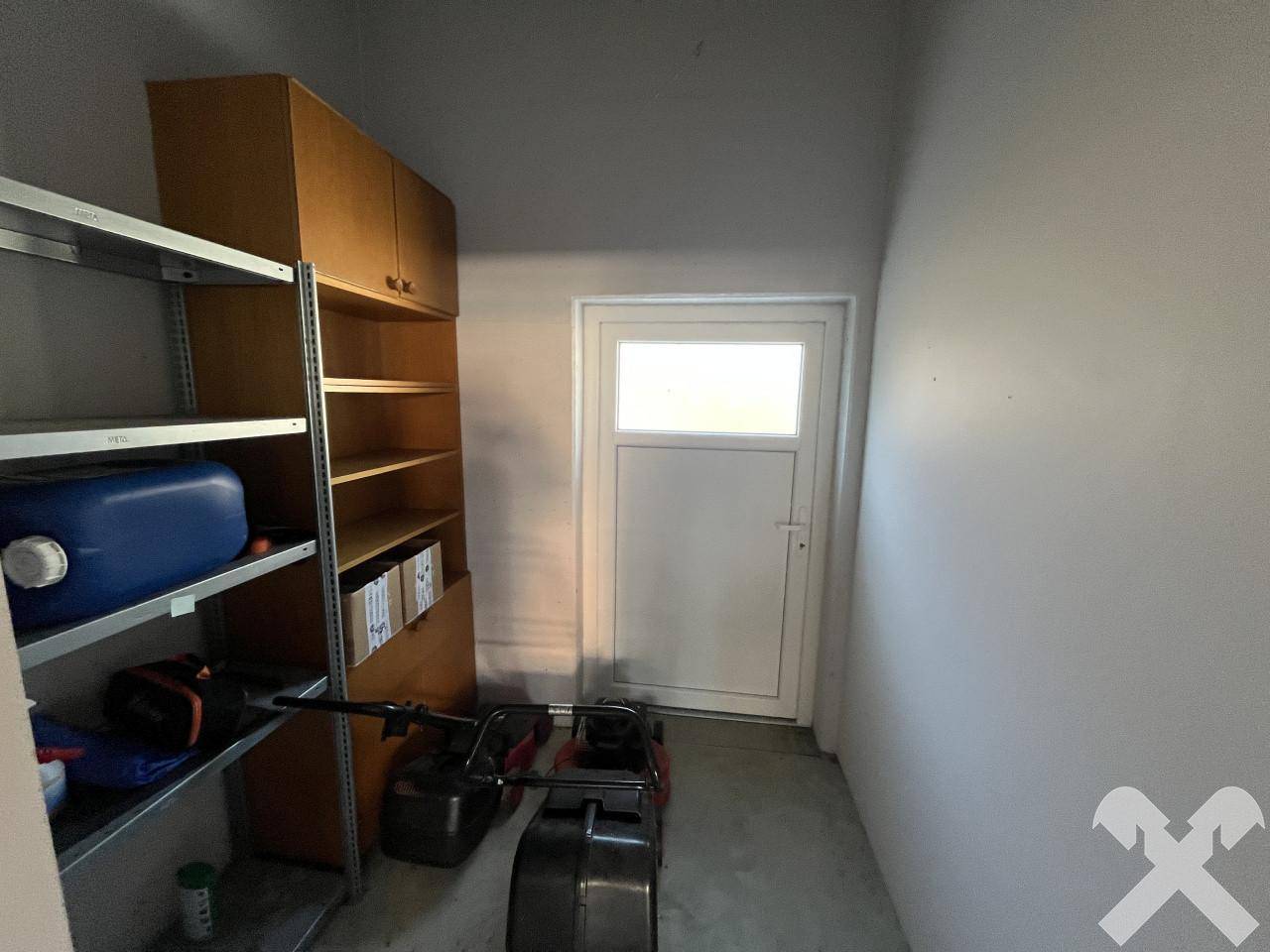 Kleiner Abstellraum mit Metallregalen, Holzschränken und einer Tür mit Fenster für Tageslicht.