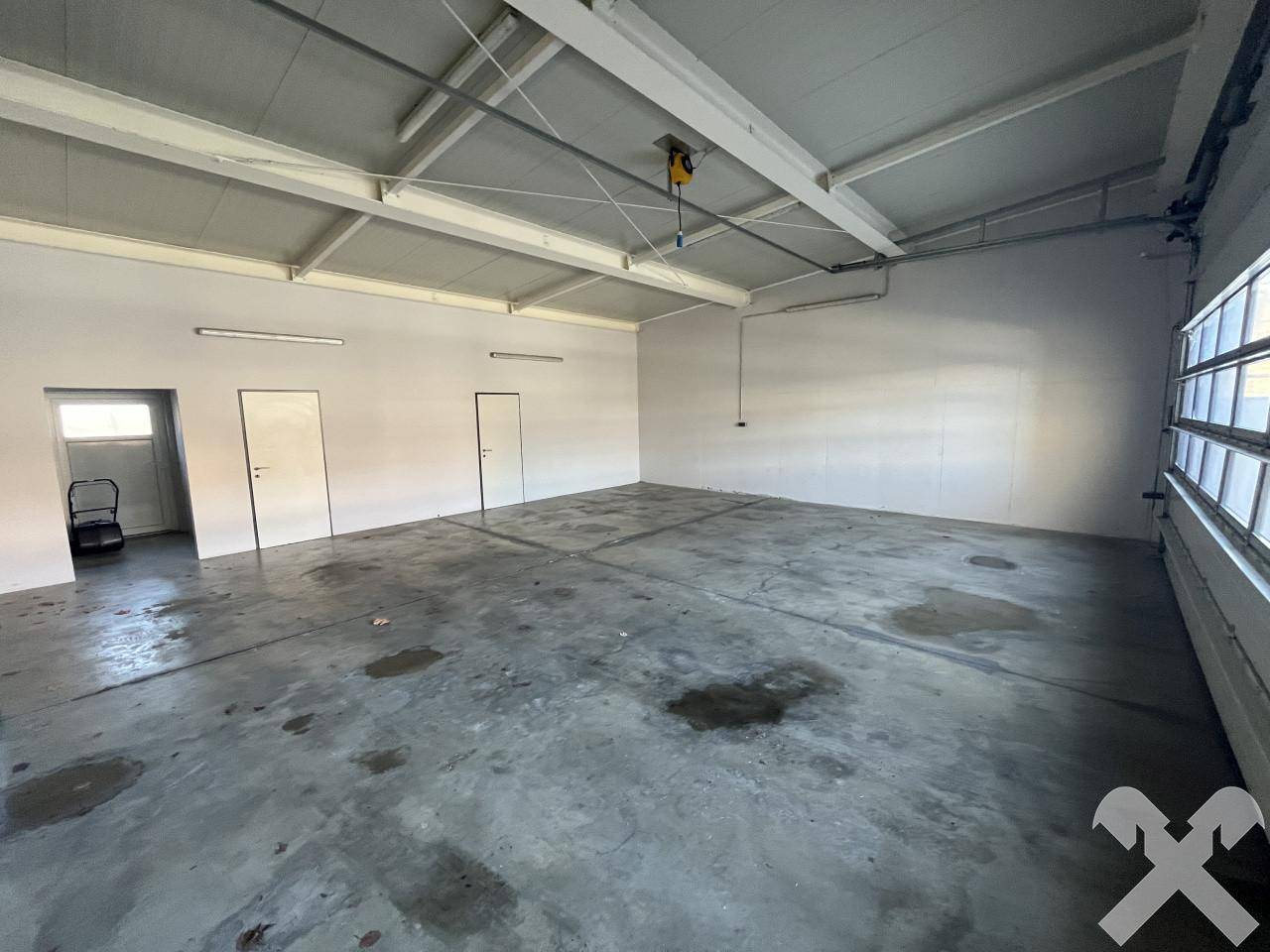 Großer, leerer Raum mit Betonboden, hohen Decken und mehreren Türen, ideal für Lagerung oder Werkstatt.
