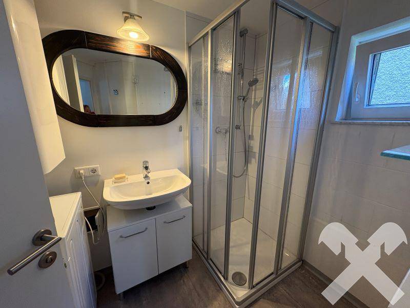 Funktionales Badezimmer mit Eckdusche, Waschbeckenunterschrank und Waschmaschine, hell gefliest.