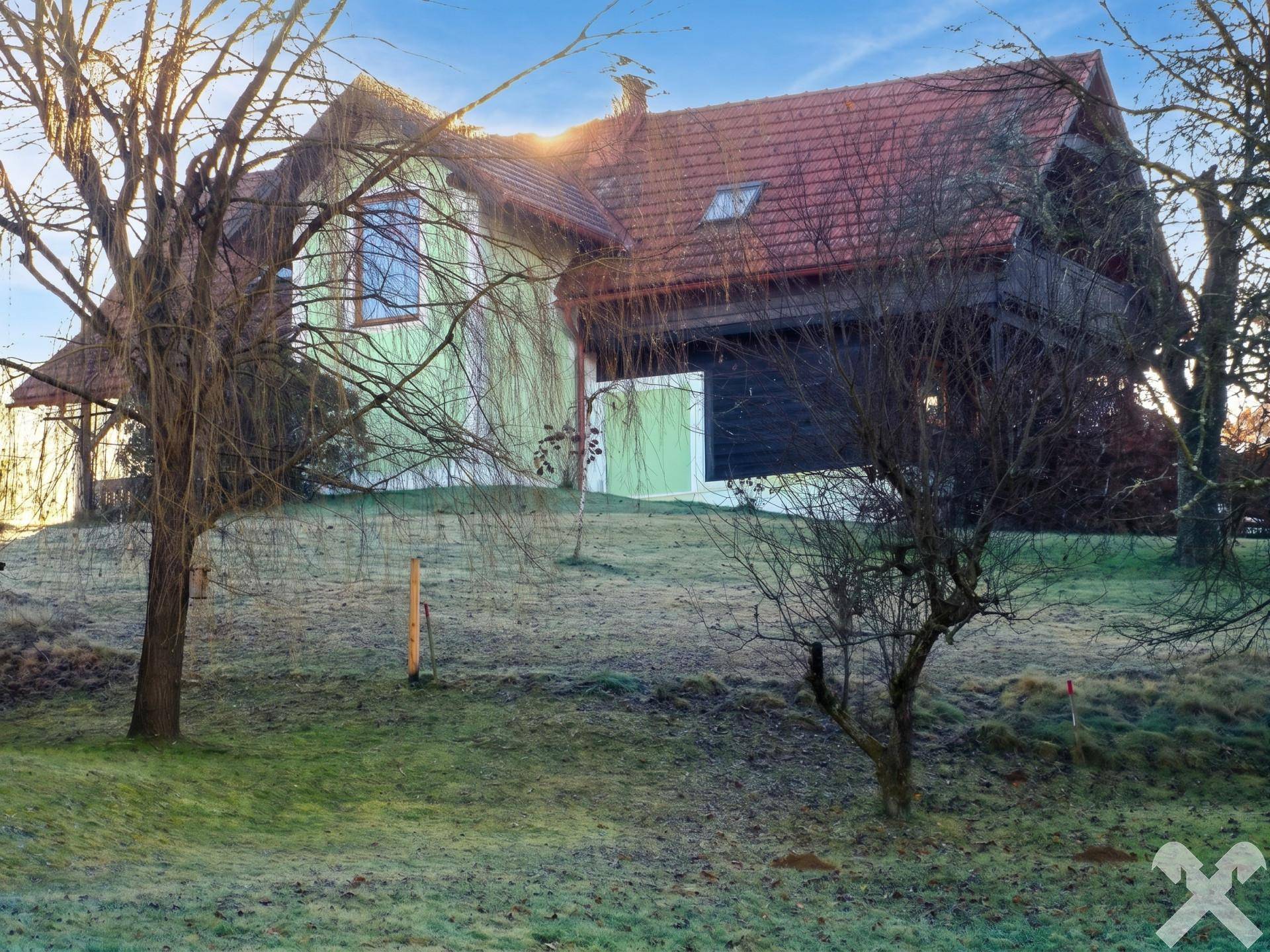 Haus mit hellgrüner Fassade und rotem Ziegeldach, umgeben von Bäumen in einer ländlichen Umgebung.