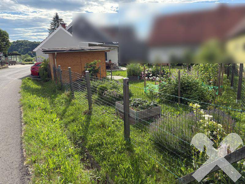 Weitläufiger Gartenbereich mit Zaun, Holzschuppen und Blick auf das Haus, umgeben von viel Grün.