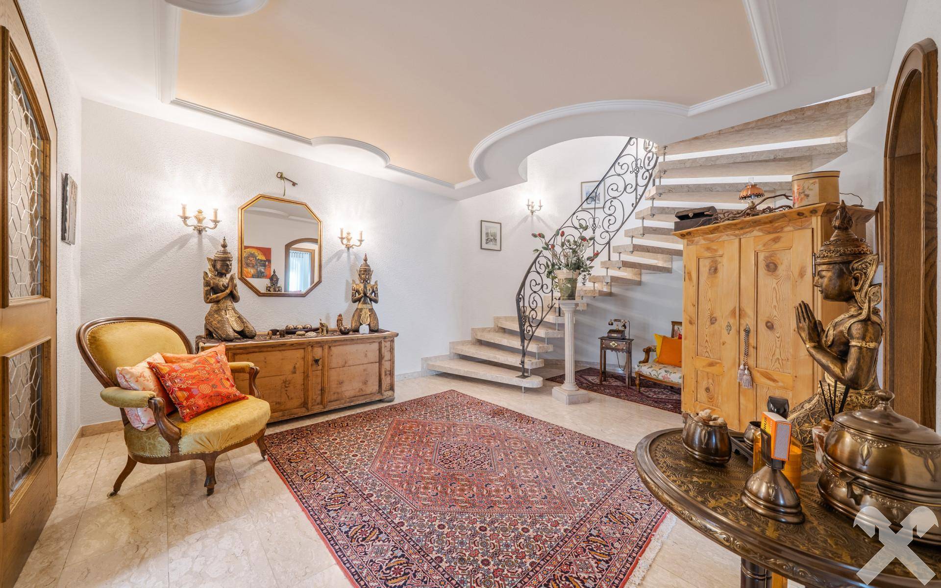 Elegante Eingangshalle mit Marmorboden, geschwungener Treppe und traditionellen Holzmöbeln.