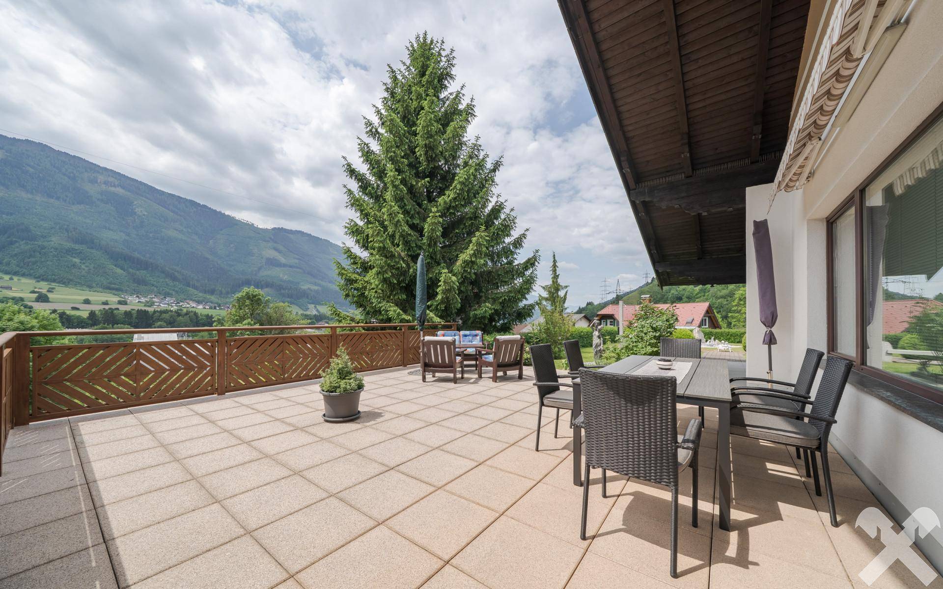 Große Sonnenterrasse mit Bergblick, Essbereich und Liegestühlen, ideal zum Entspannen im Freien.