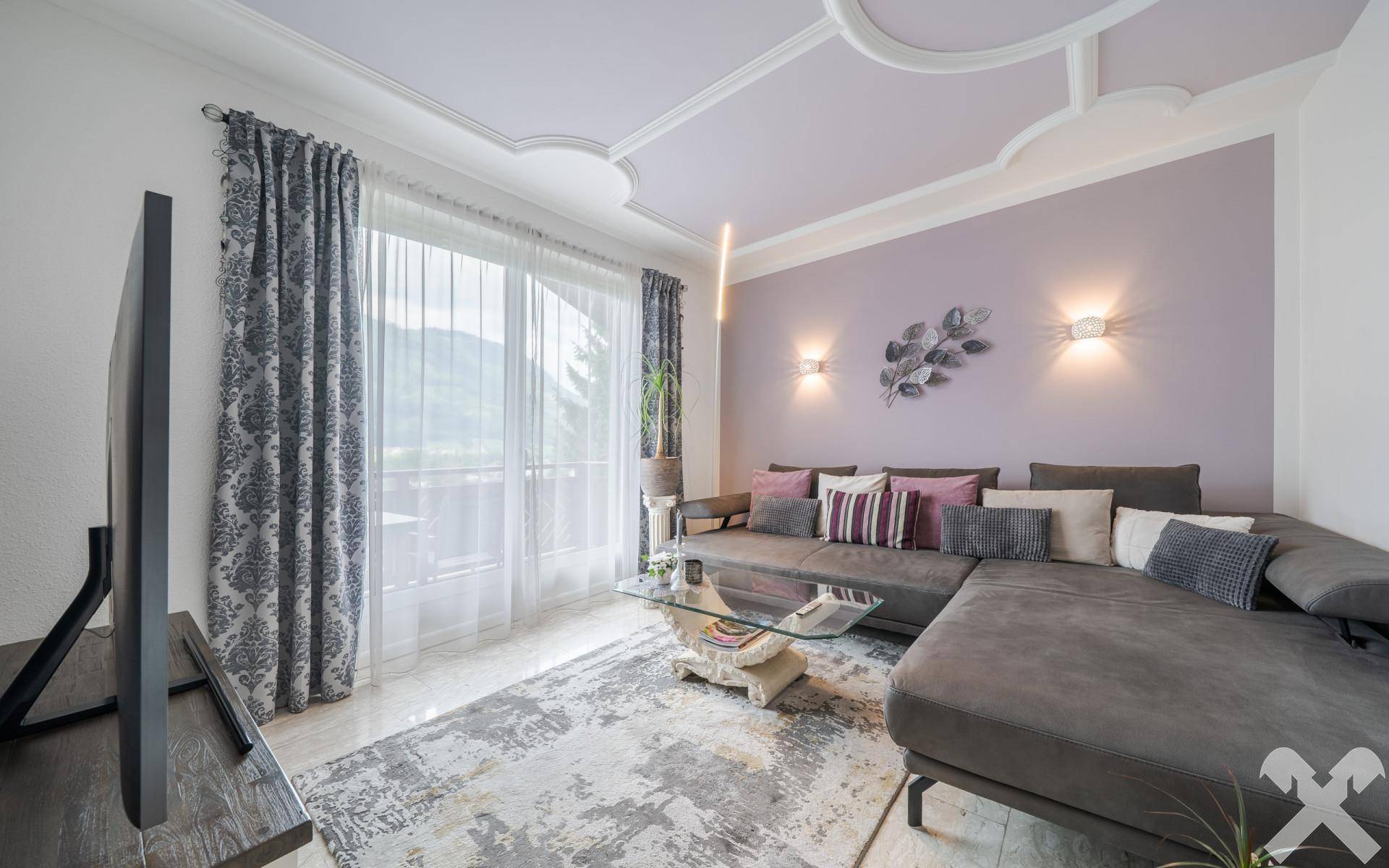 Gemütliches Wohnzimmer mit großem Ecksofa, dekorativer Decke und Zugang zu einem Balkon.