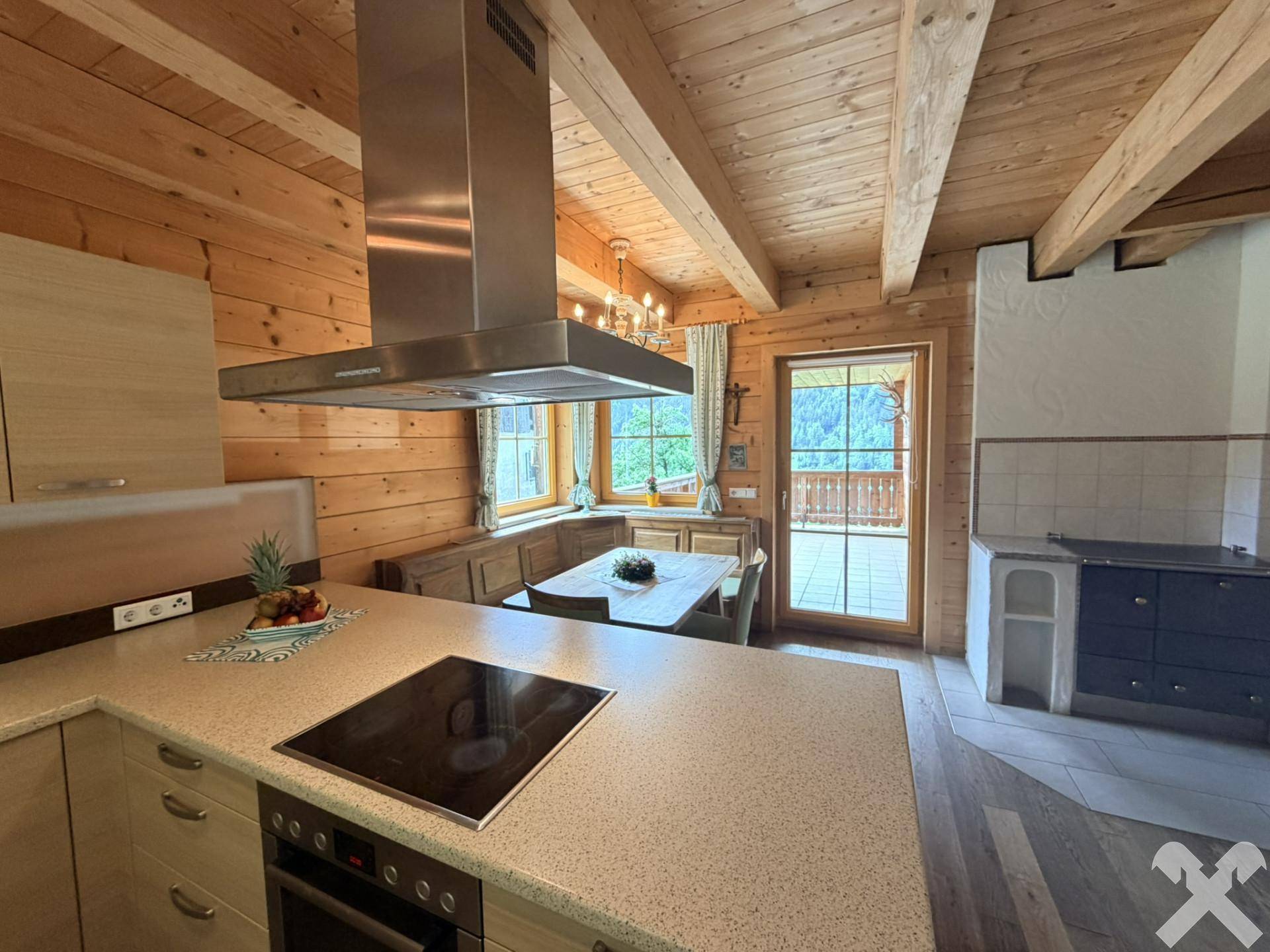 Offene Küche mit Essbereich, traditionellem Holzofen und Zugang zum Balkon mit Bergblick.