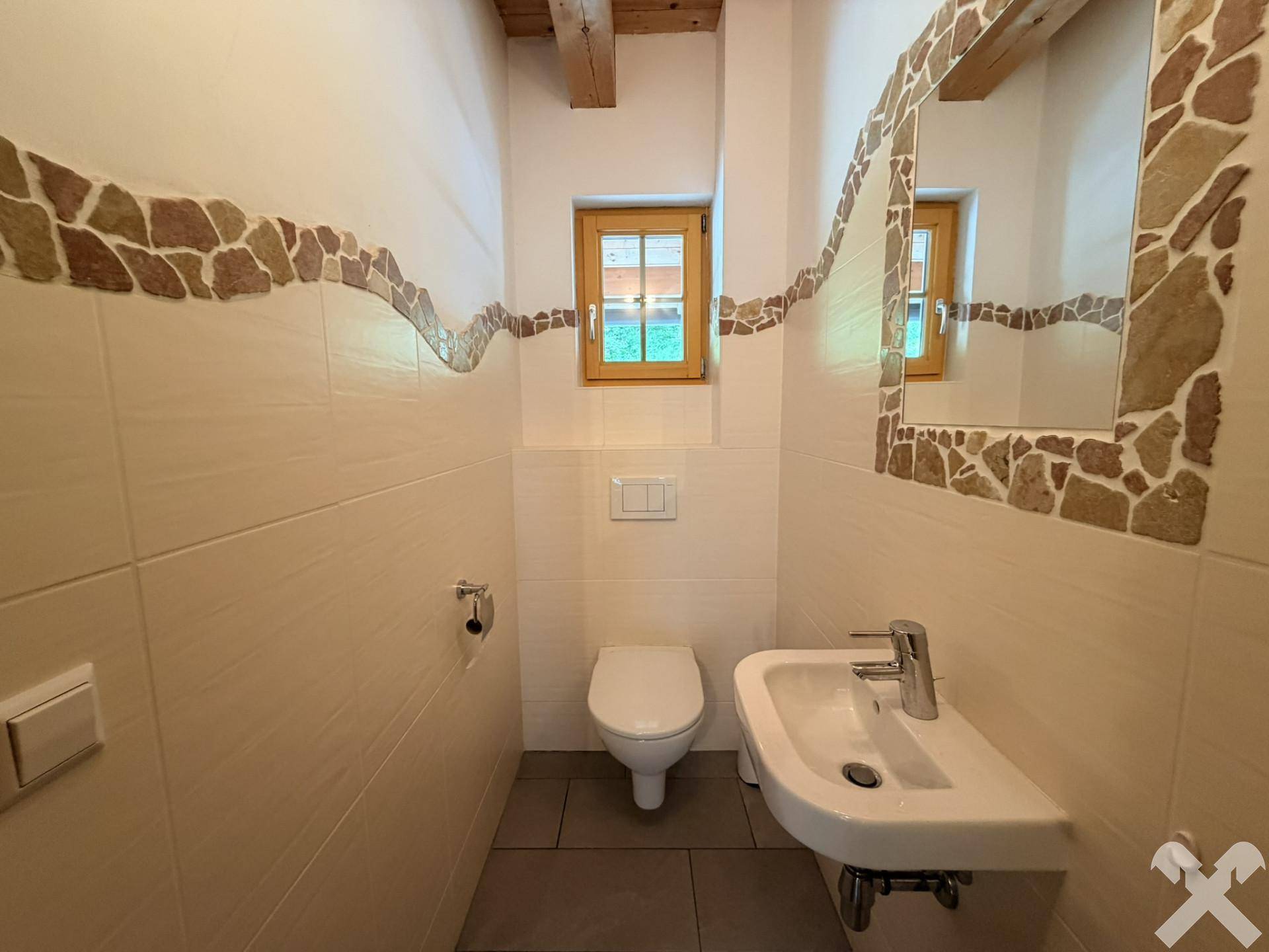 Kleines Gäste-WC mit Fenster, Wand-WC und Waschbecken, dekoriert mit Steinakzenten.