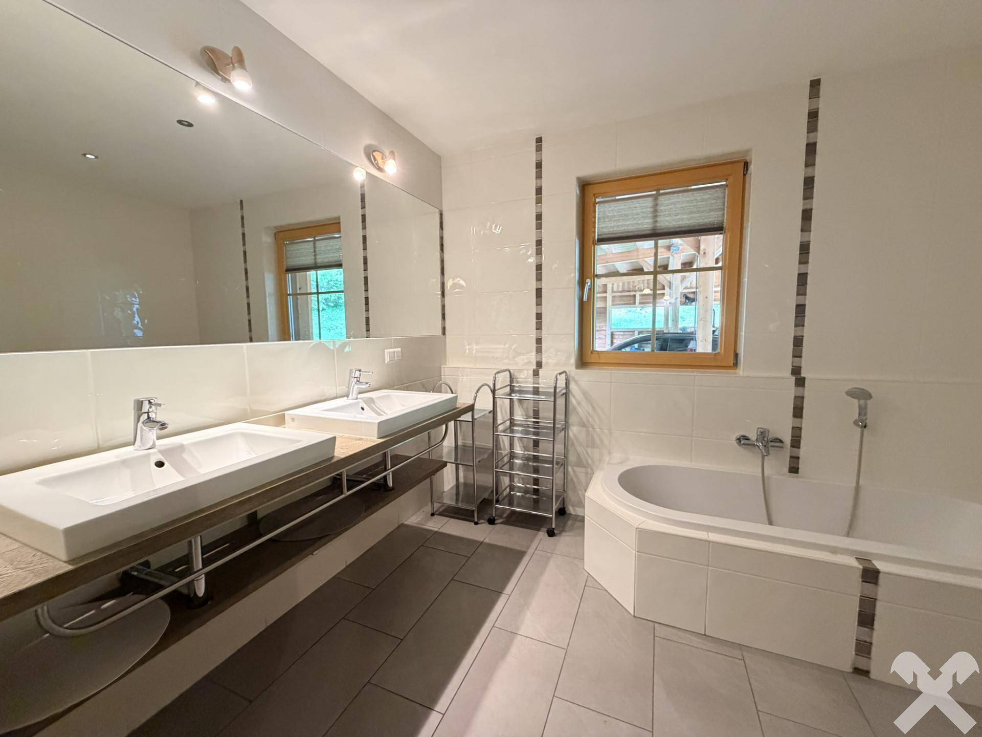Modernes Badezimmer mit Doppelwaschbecken, Badewanne und Fenster, hell gefliest.