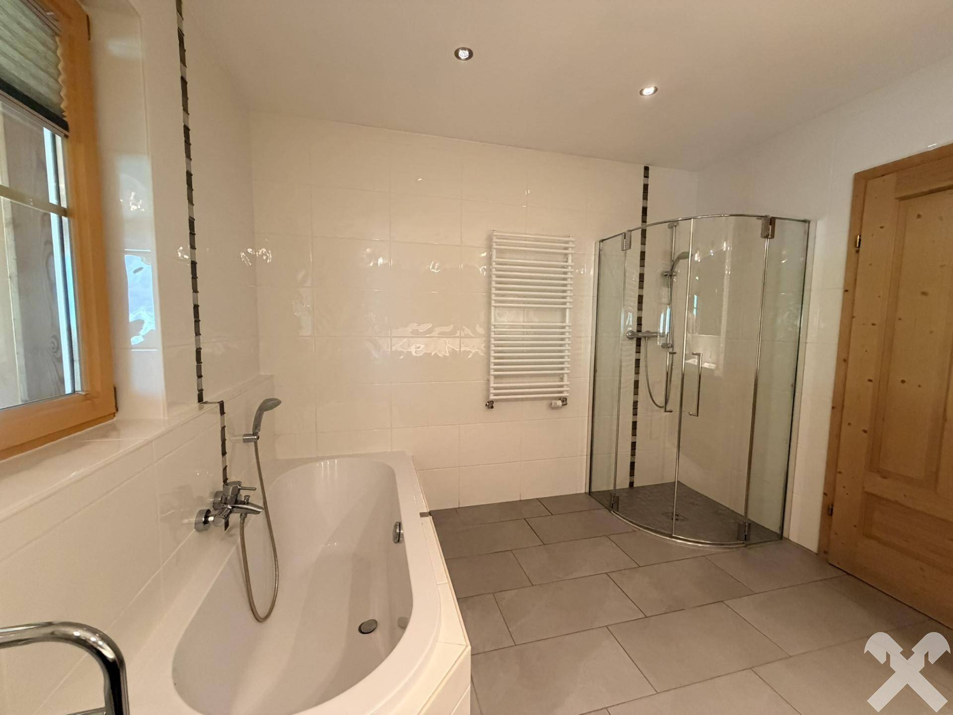 Helles Badezimmer mit Badewanne, Duschkabine und beheiztem Handtuchhalter, modern gefliest.