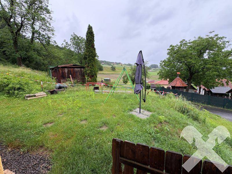 Grüner Gartenbereich mit Schaukelgestell, Sonnenschirm und Blick auf die Landschaft.