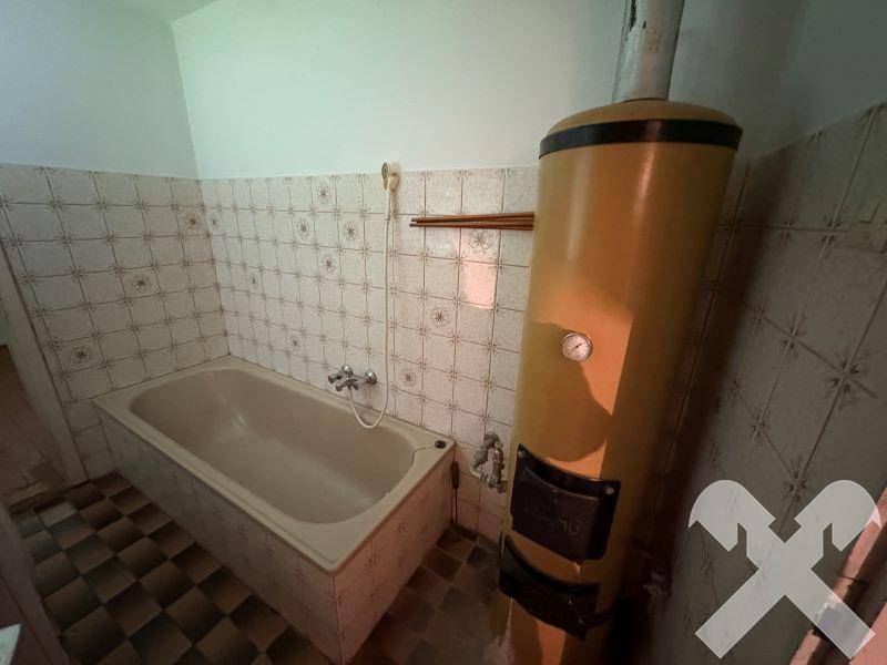 Veraltetes Badezimmer mit Badewanne, gefliesten Wänden und einem großen Warmwasserboiler.