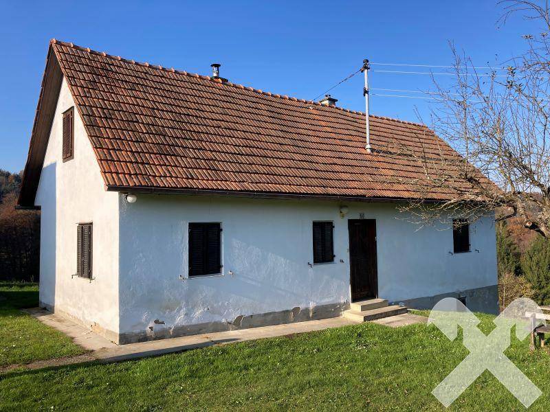 Vorderansicht des kleinen weißen Hauses mit rotem Ziegeldach, dunklen Fensterläden und einfacher Holztür.