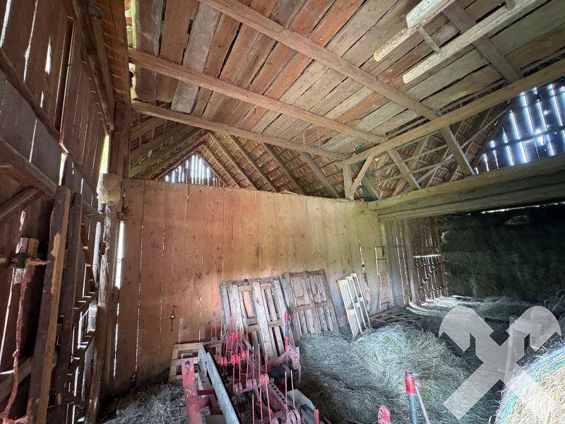 Geräumiger Innenraum einer Scheune mit Holzbalken, Heuballen und landwirtschaftlichen Geräten.