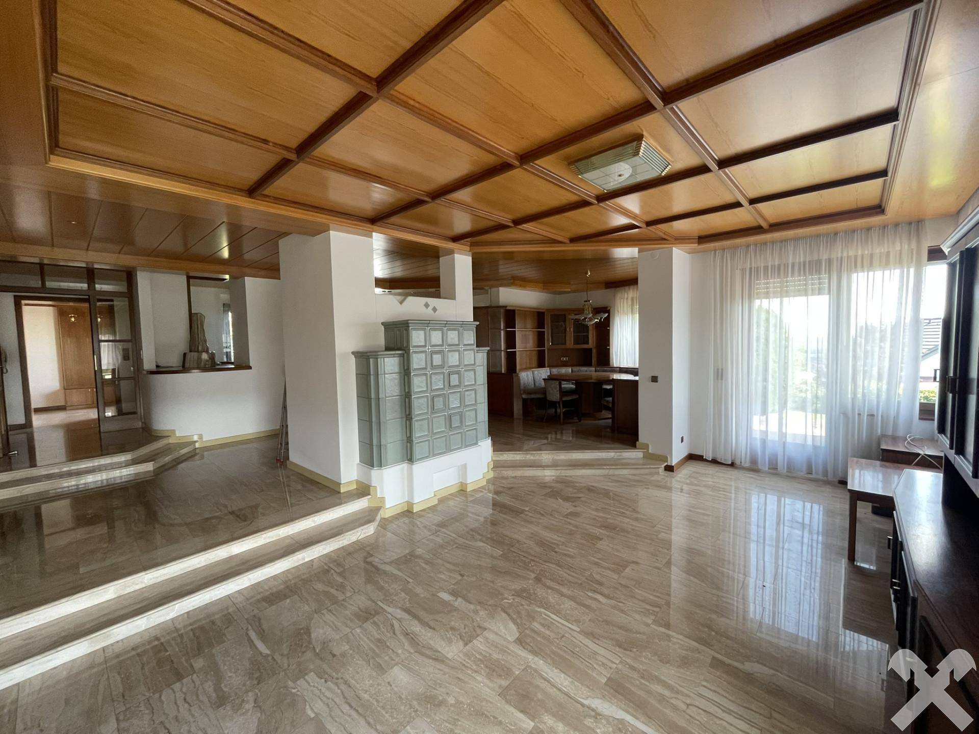 Geräumiges Wohnzimmer mit glänzendem Marmorboden, Holzkassettendecke und traditionellem Kachelofen.
