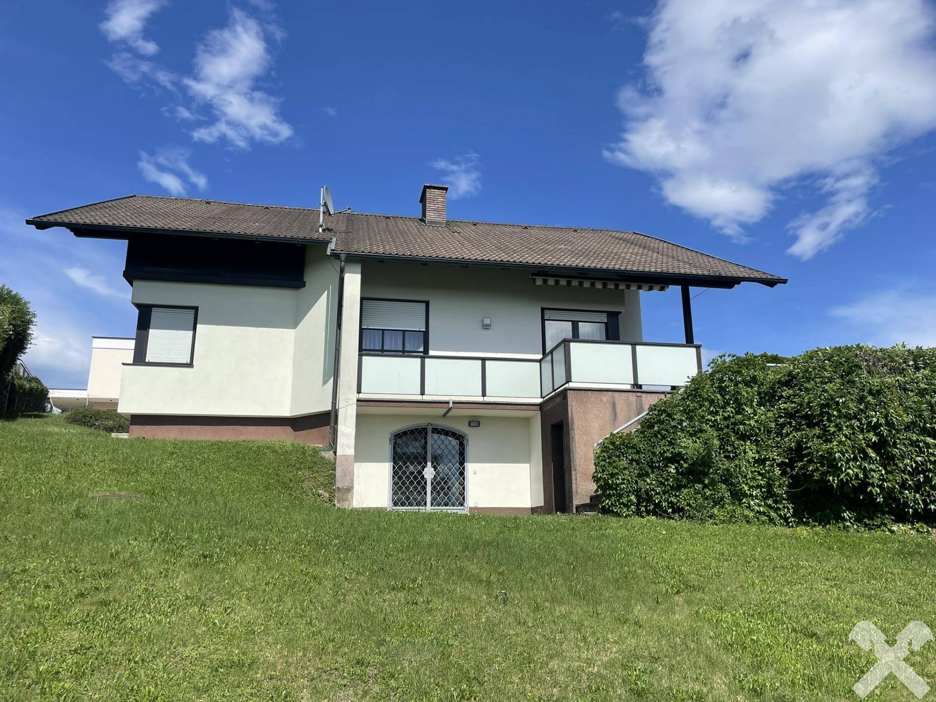 Seitenansicht des Hauses mit Balkon und Zugang zum Gartenbereich unter blauem Himmel.