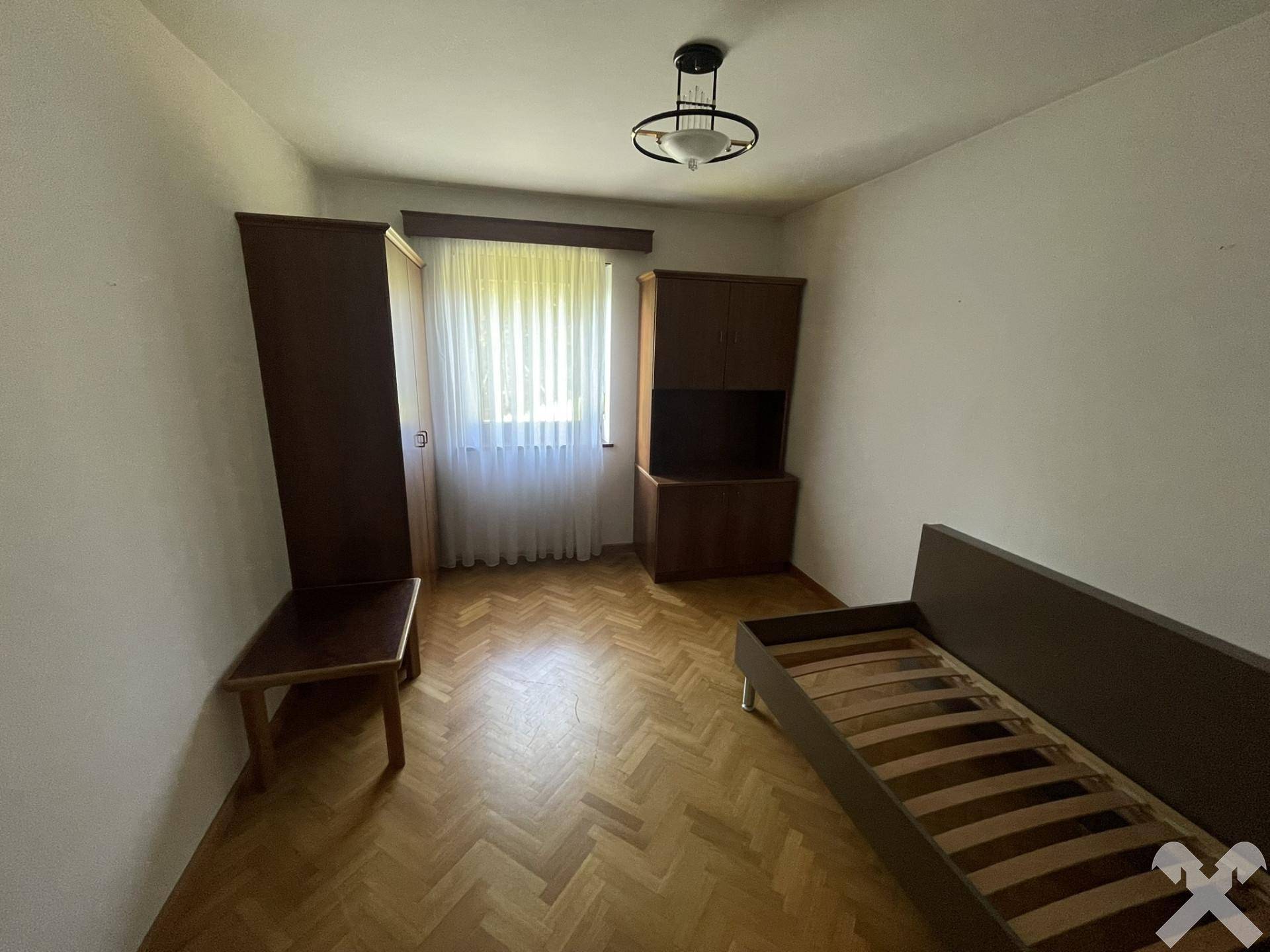 Schlafzimmer mit Parkettboden, schlichten Holzmöbeln und einem Fenster mit Vorhängen.