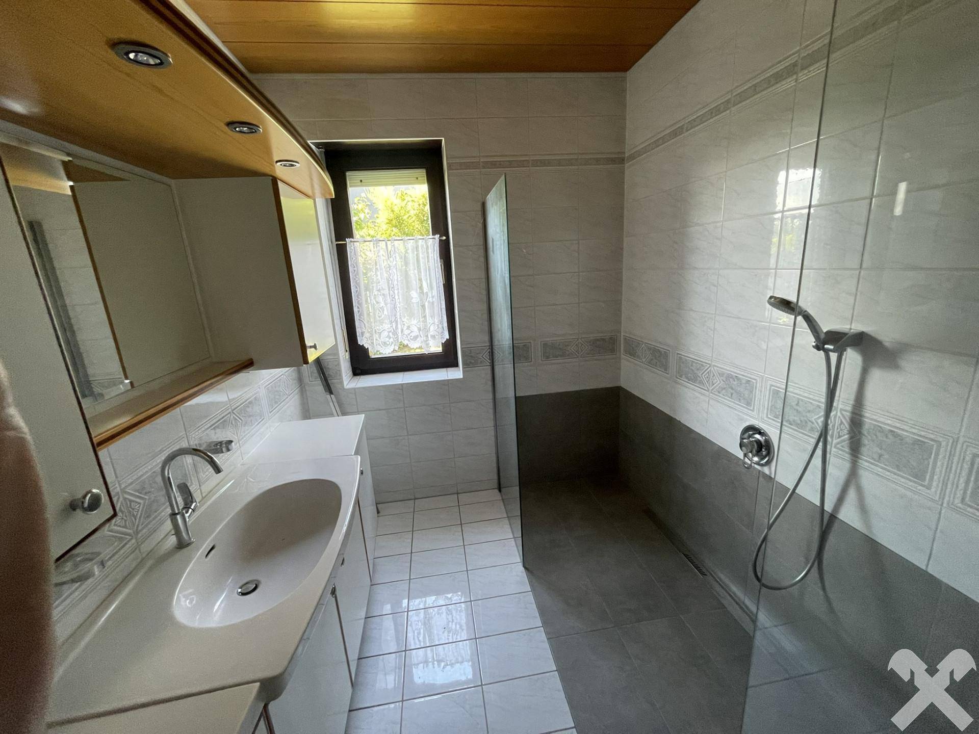 Modernes Badezimmer mit grauen und weißen Fliesen, Einzelwaschbecken und einer begehbaren Dusche.