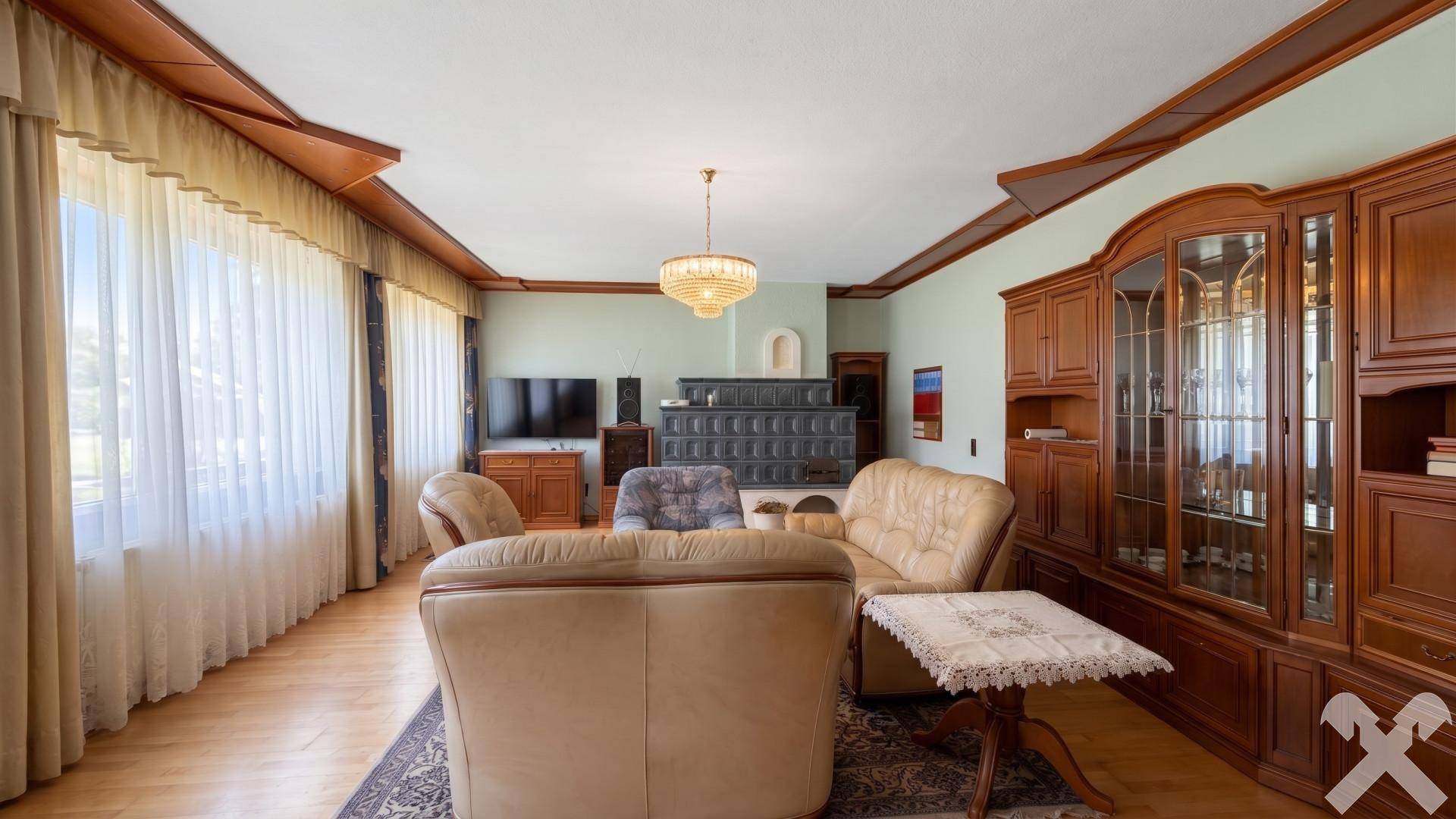Geräumiges Wohnzimmer mit Kachelofen, Ledersofas, Holzvertäfelung und großen Fenstern.