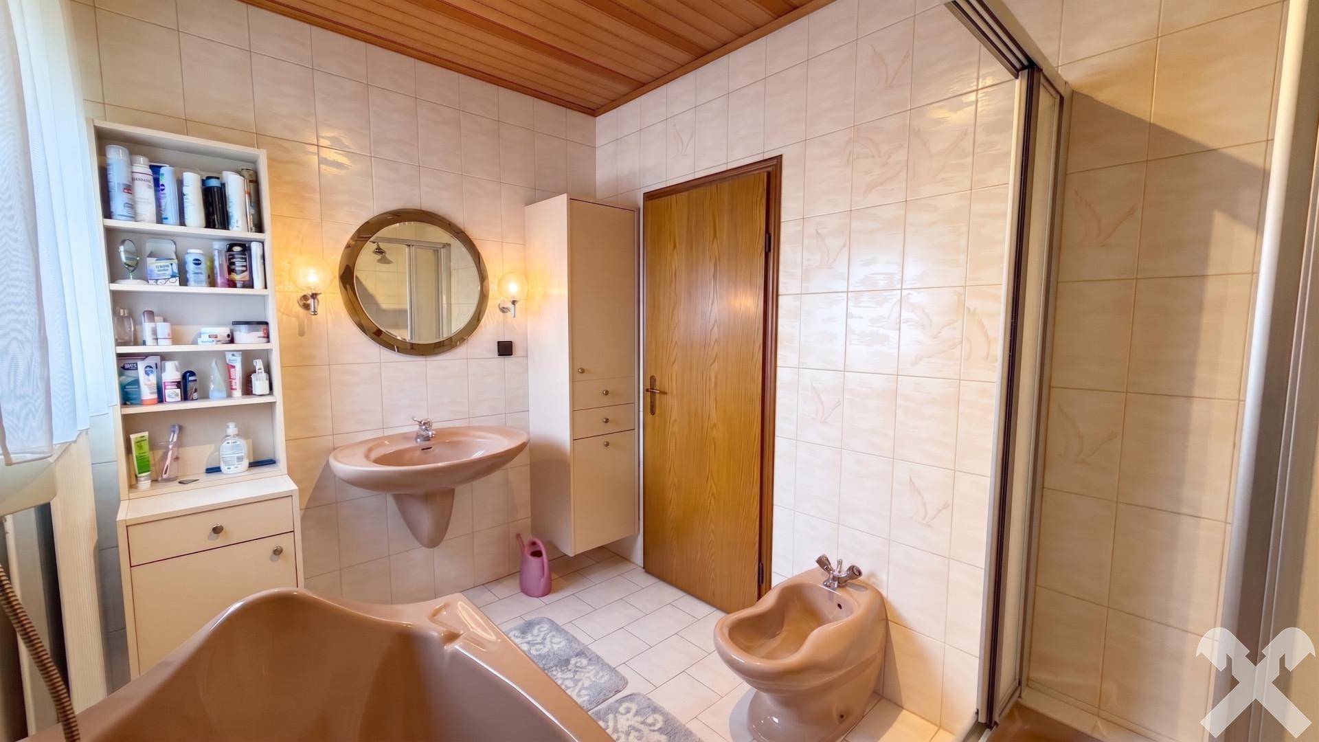 Badezimmer im Stil der 80er Jahre mit pfirsichfarbenen Sanitärobjekten, Fliesen und Holzdecke.