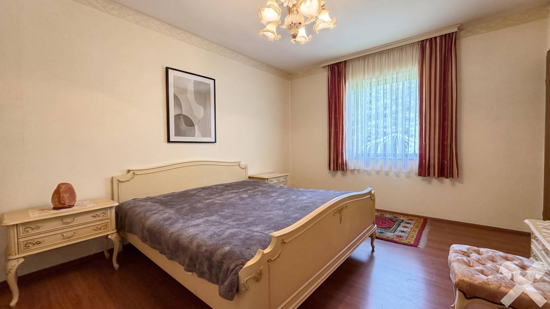 Gemütliches Schlafzimmer mit klassischem Bett, Nachttischen und Fenster mit rotem Vorhang.