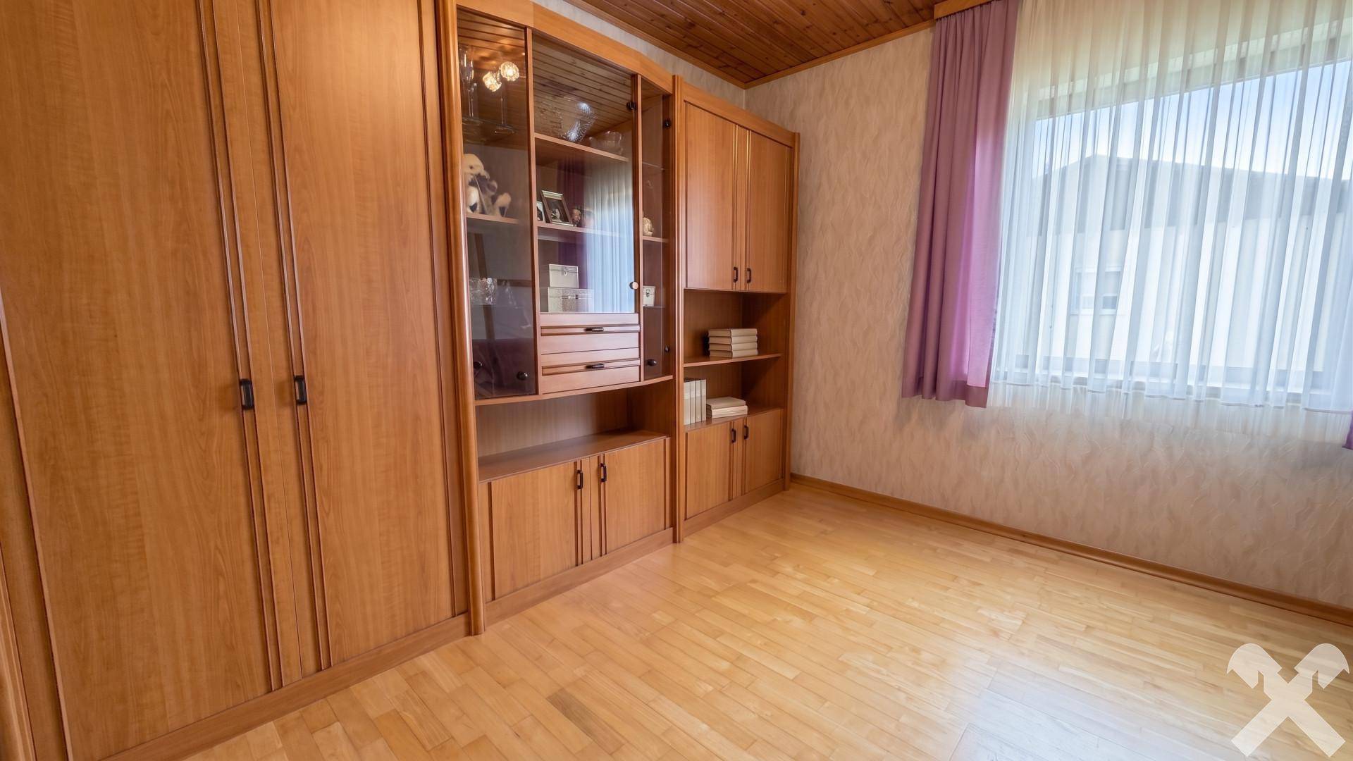 Helles Zimmer mit Einbauschränken aus Holz, Holzdecke und Fenster mit lila Vorhang.