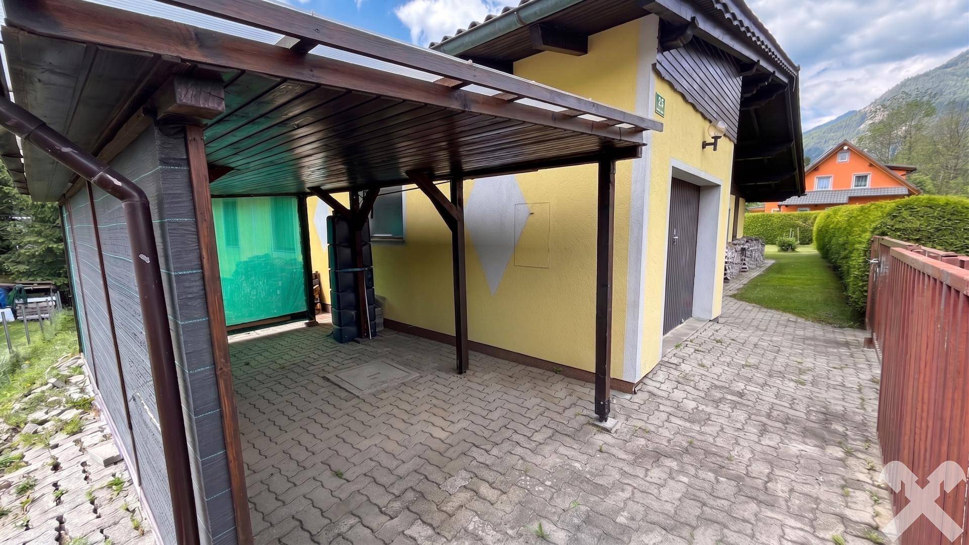 Überdachter Carport und gepflasterte Zufahrt zum Garagentor des gelben Hauses.