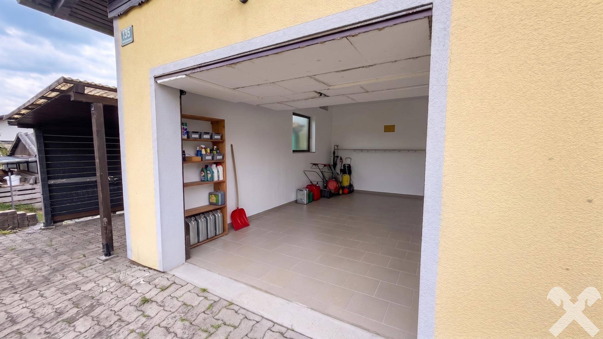 Geräumige Garage mit Fliesenboden, Fenster und Regalen für Werkzeuge und Geräte.