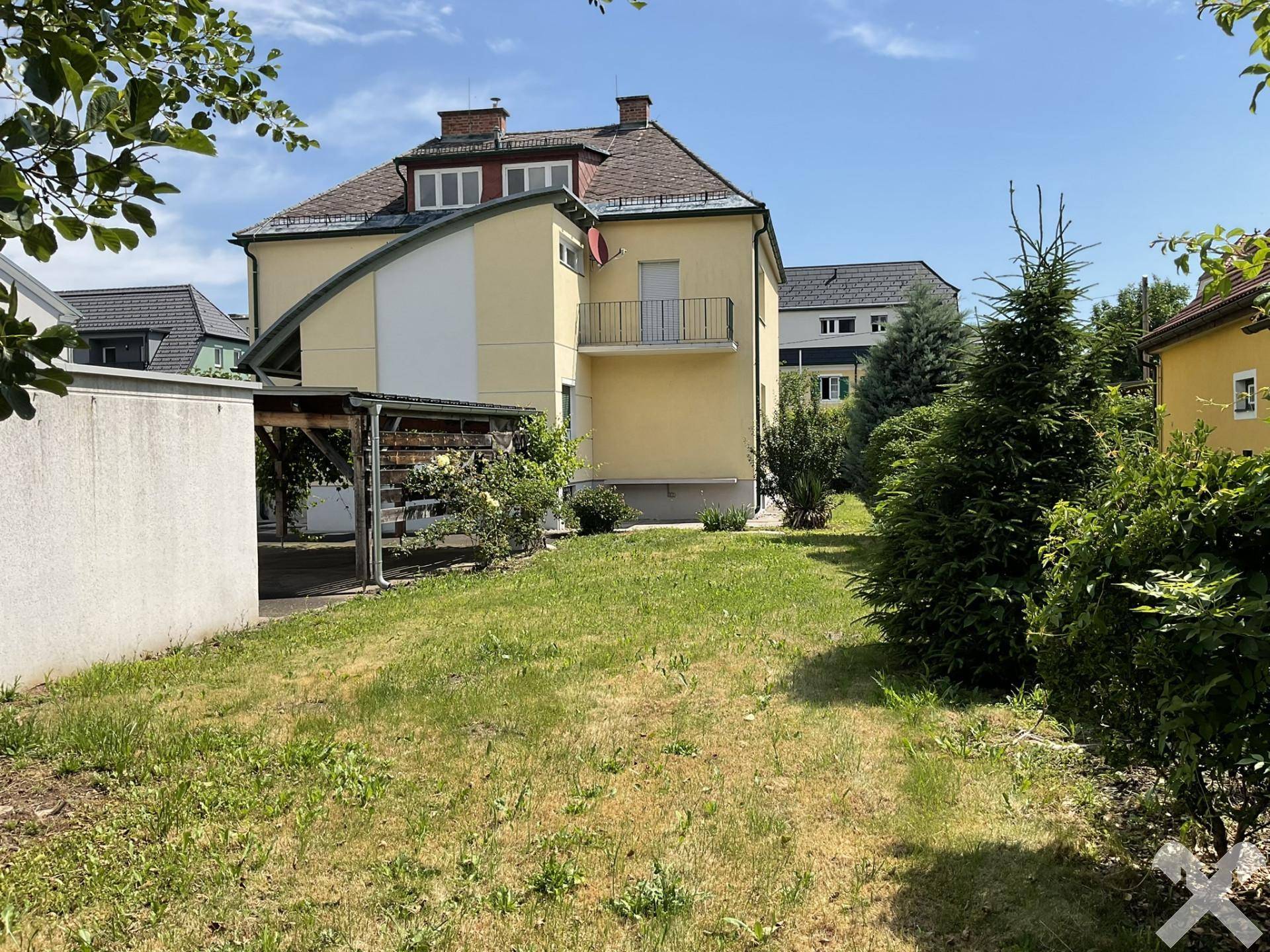 Hinteransicht des Hauses mit Rasenfläche und Bäumen unter blauem Himmel.