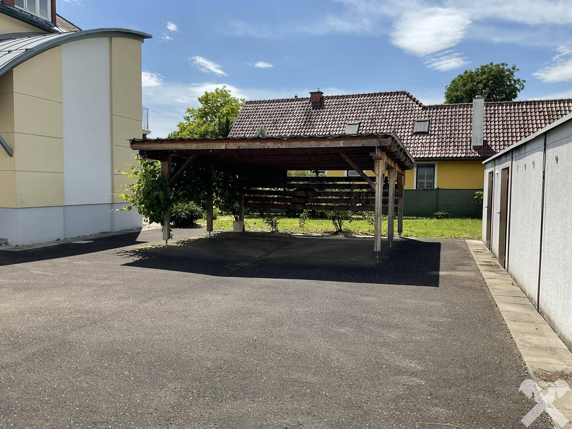 Überdachter Holzcarport auf asphaltiertem Parkplatz neben dem Gebäude.