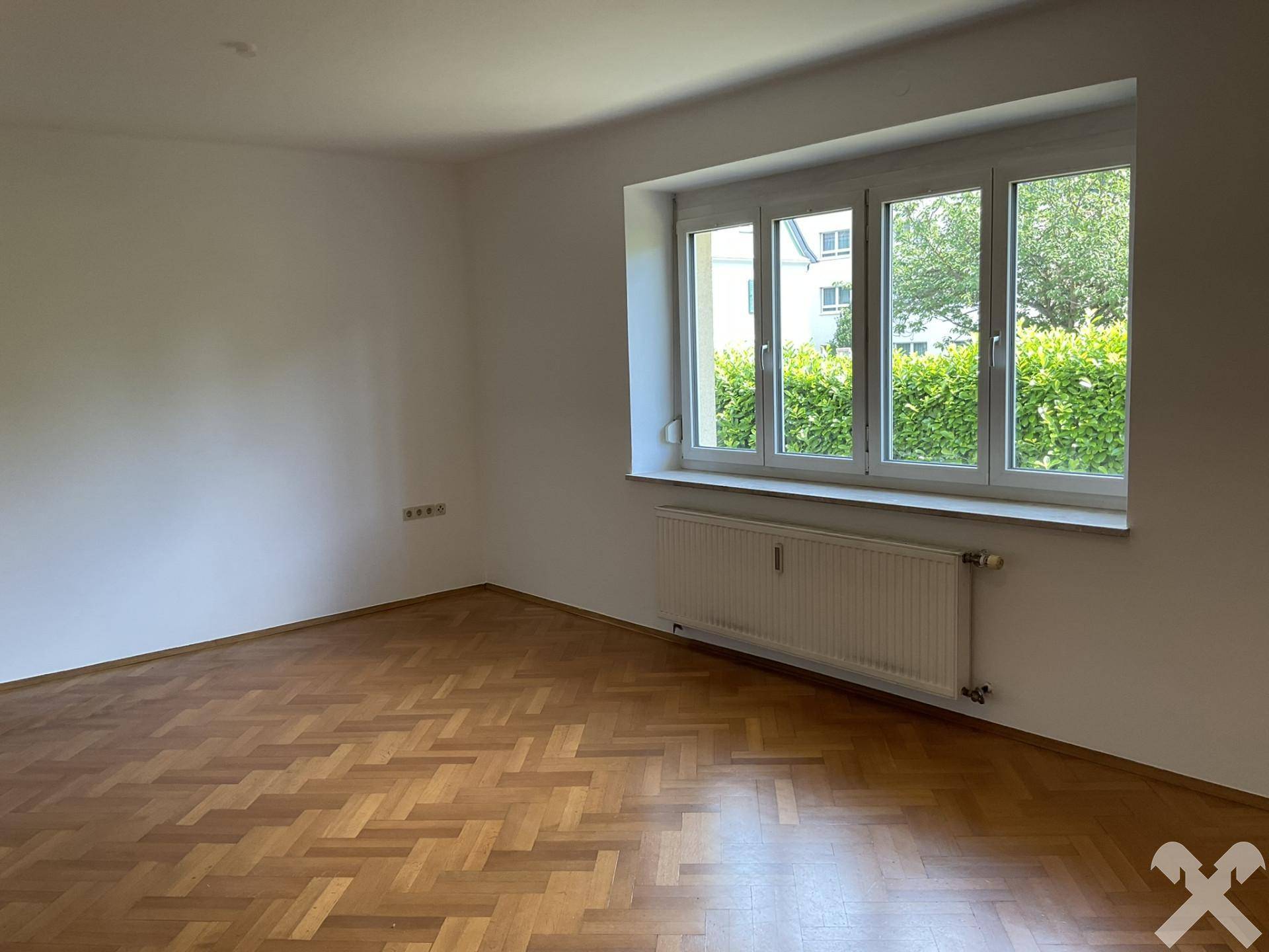 Helles Zimmer mit Parkettboden und Fensterfront mit Blick auf die Umgebung.