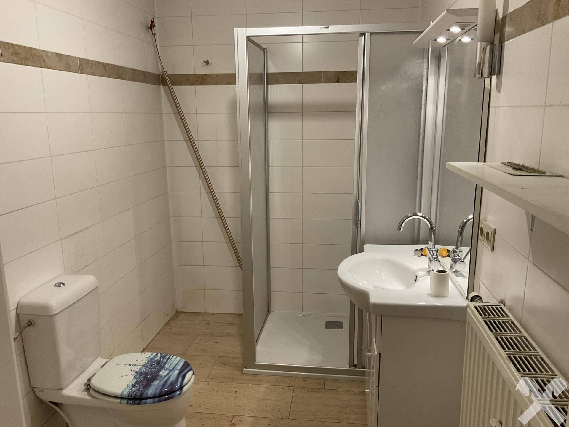 Badezimmer mit Duschkabine, Waschbecken und WC, hell gefliest.
