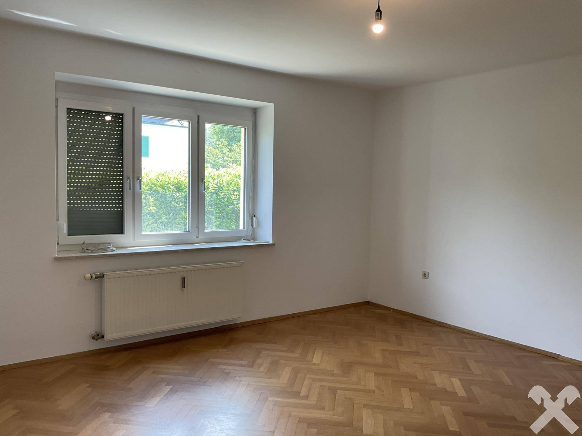 Geräumiges Schlafzimmer mit Holzparkettboden und Blick ins Grüne.