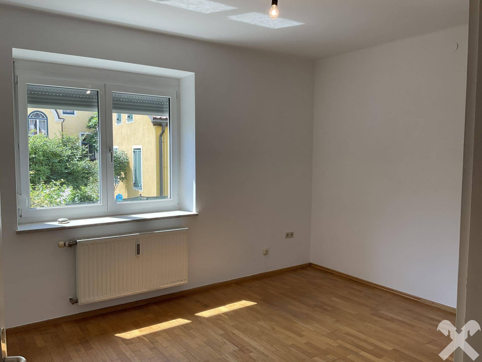 Helles Schlafzimmer mit Fischgrätparkett, großem Fenster und Heizkörper.