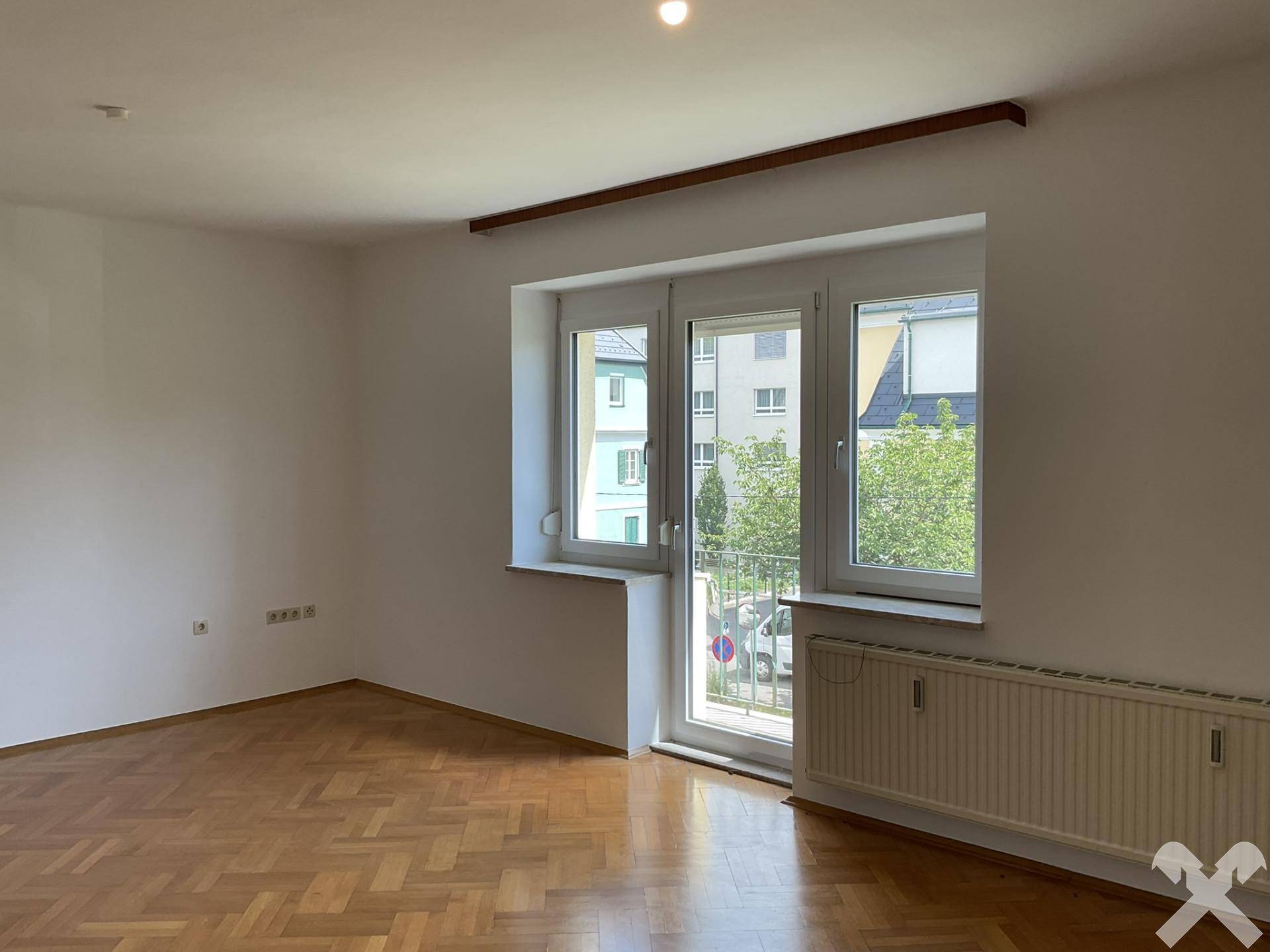 Helles Zimmer mit Parkettboden und Balkontür, die viel Licht hereinlässt.