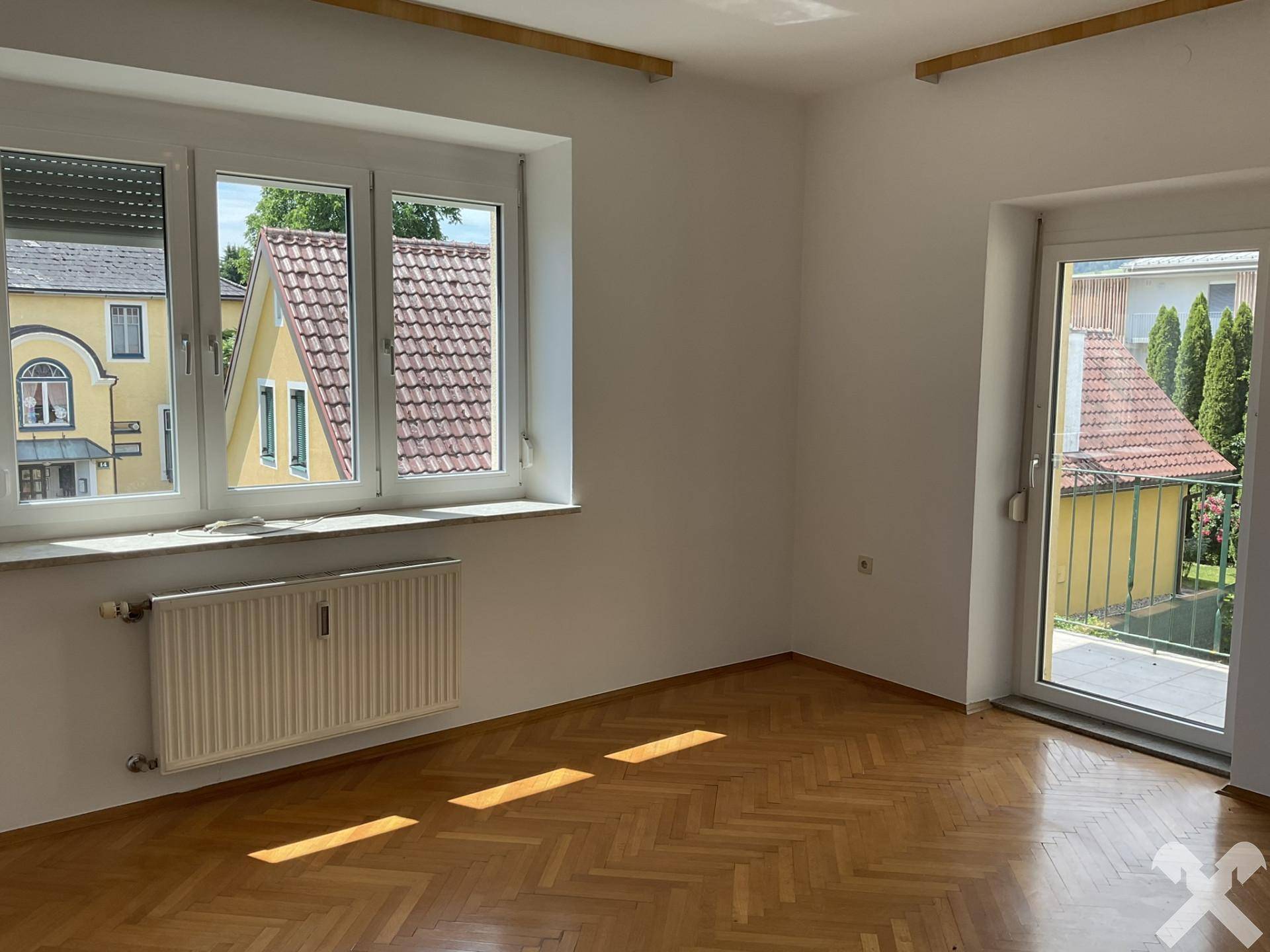 Helles Zimmer mit Parkettboden und Zugang zu einem kleinen Balkon.