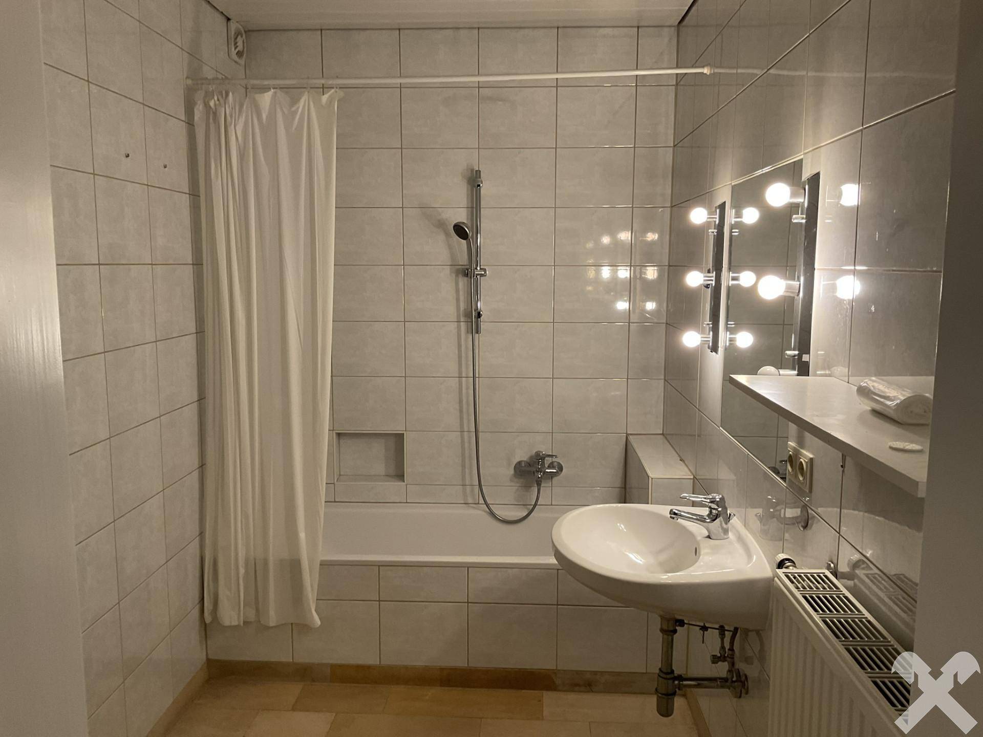 Badezimmer mit Badewanne, Duschvorhang und beleuchtetem Spiegel über dem Waschbecken.