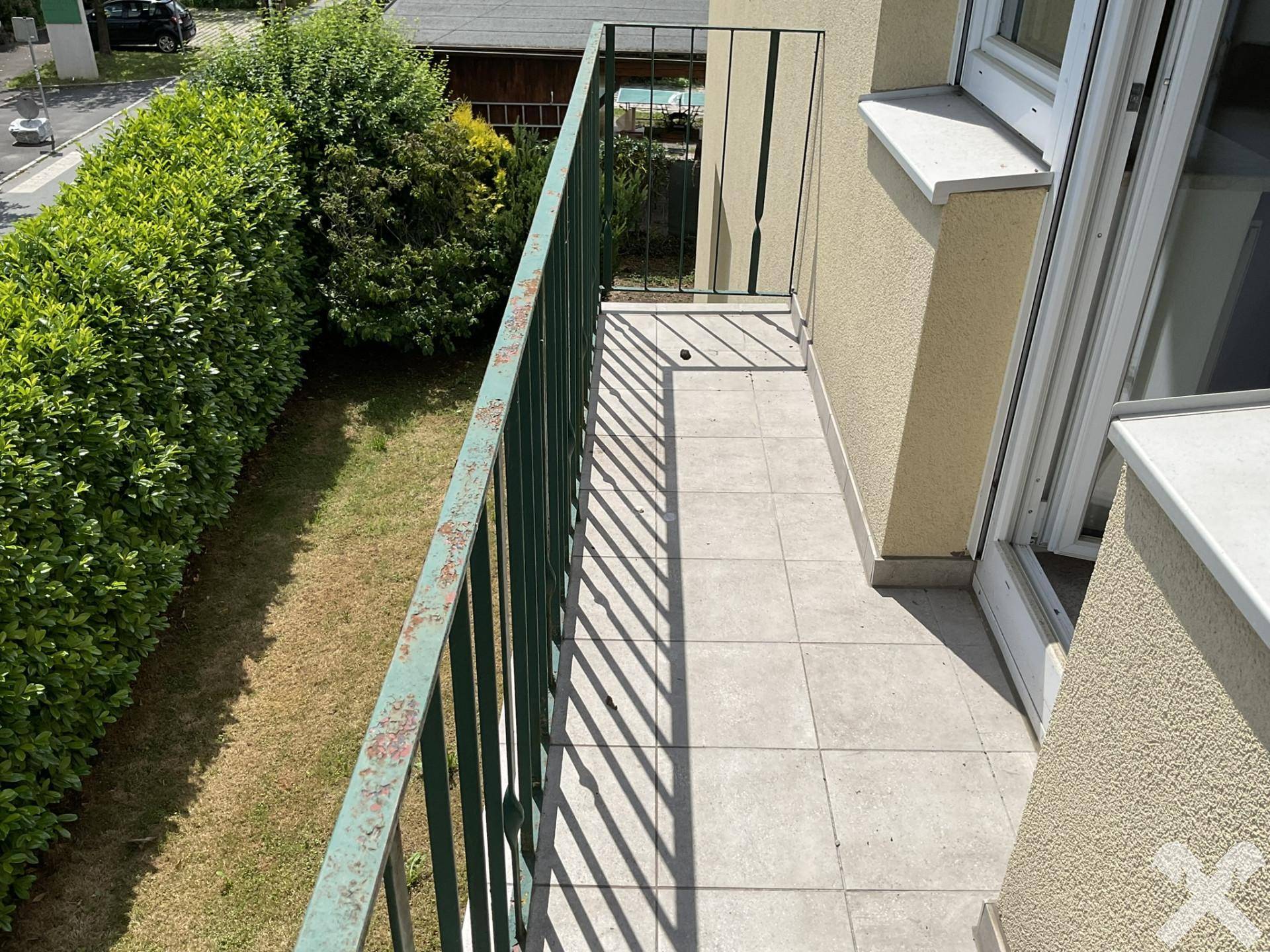 Schmaler Balkon mit Fliesenboden und Blick auf die Straße und Hecke.