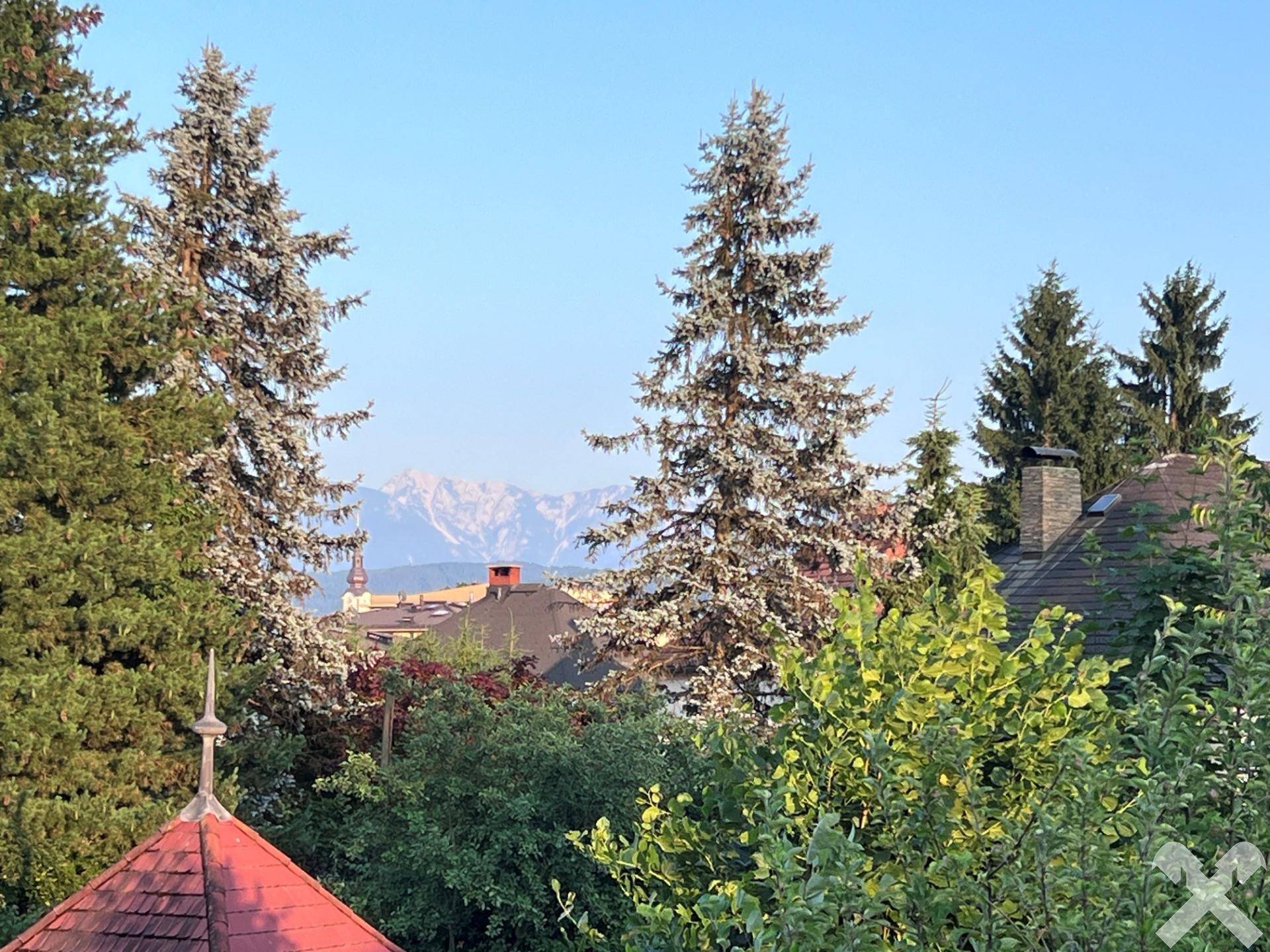 Malerischer Blick auf die Berge über Baumwipfel und Dächer der Umgebung.