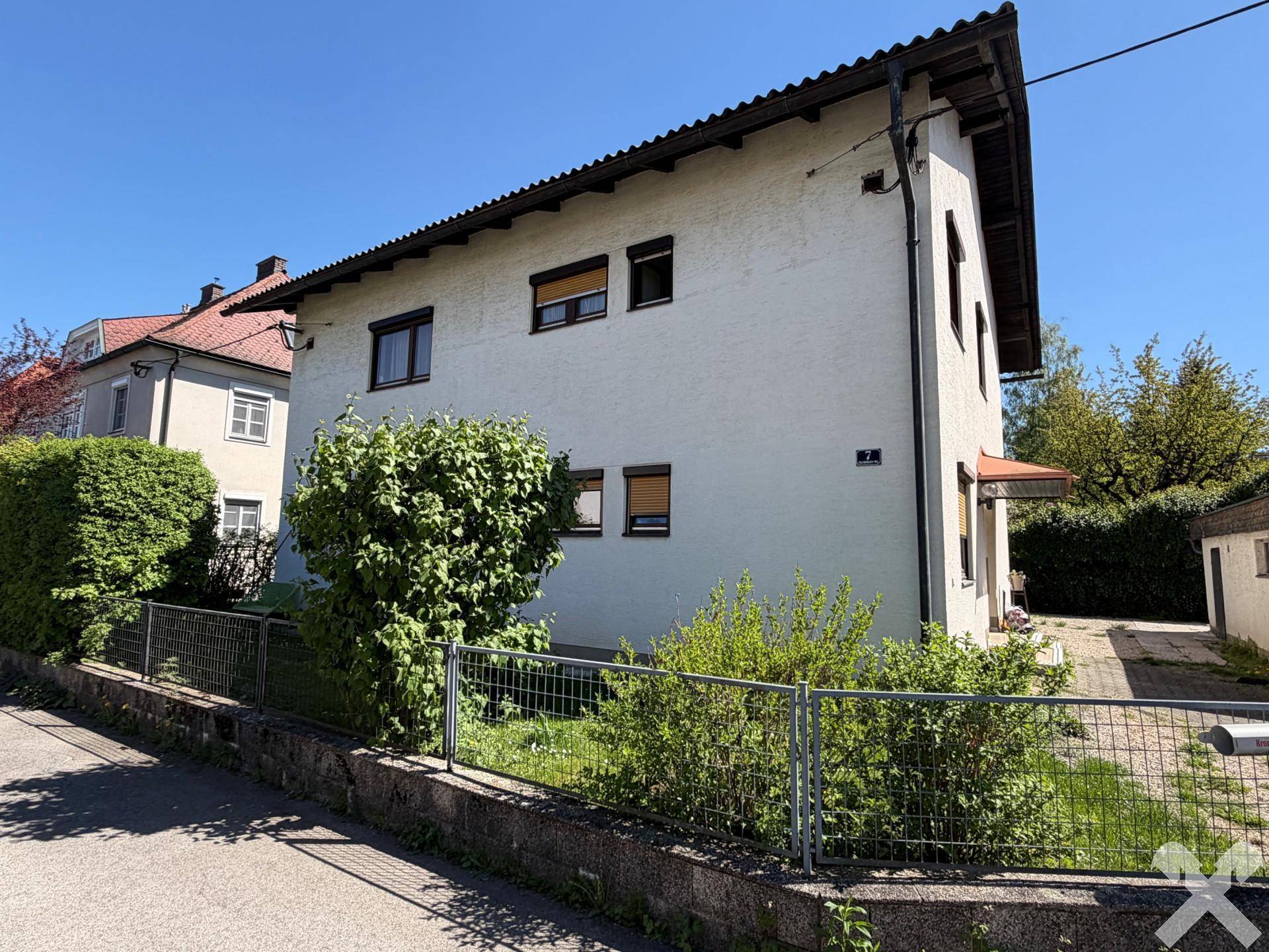Ansicht des weißen Einfamilienhauses mit gepflegtem Vorgarten und Hecke unter blauem Himmel.