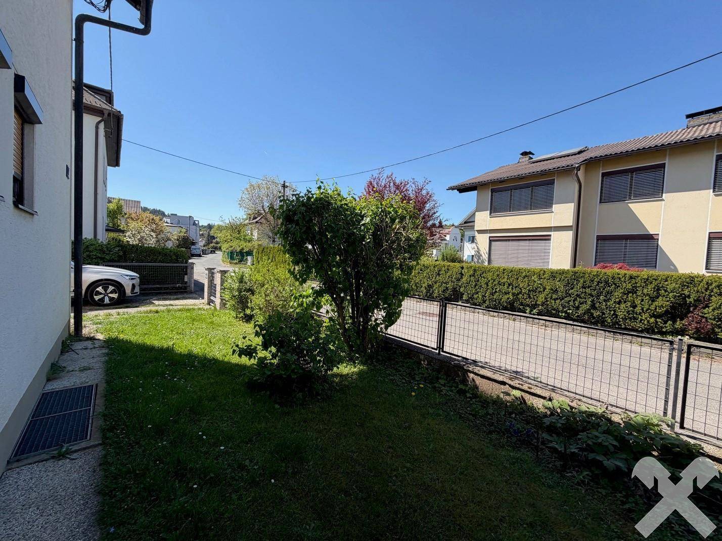 Seitlicher Gartenbereich mit Rasen, Sträuchern und Blick auf die Nachbarschaft.