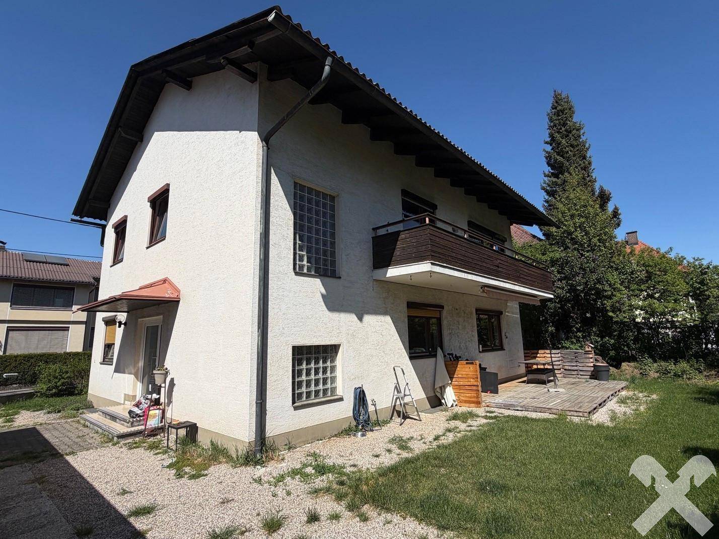 Seitenansicht des Hauses mit Balkon, Gartenbereich und Kiesfläche unter blauem Himmel.