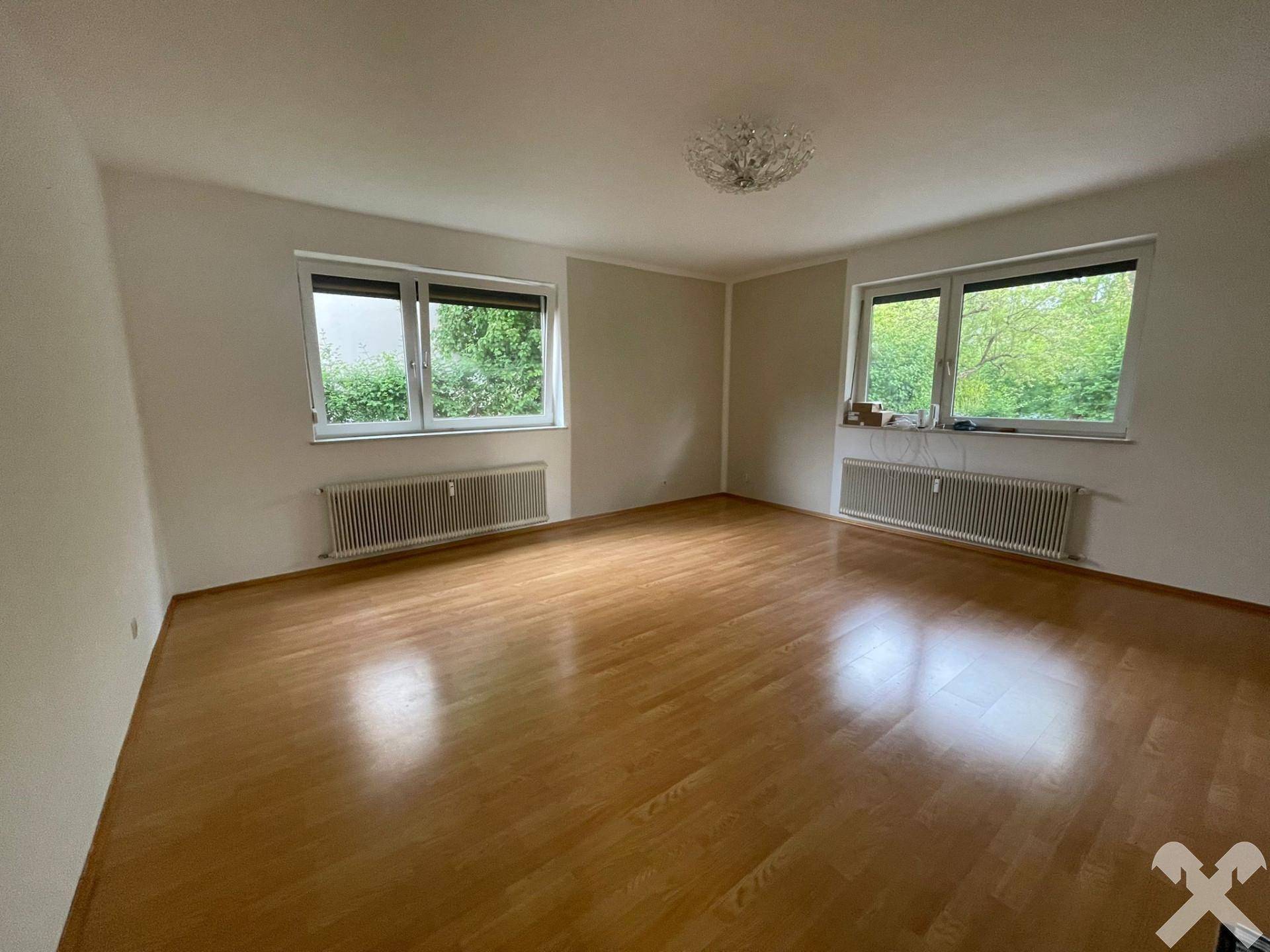 Helles, leeres Zimmer mit Parkettboden, großen Fenstern und Heizkörpern.