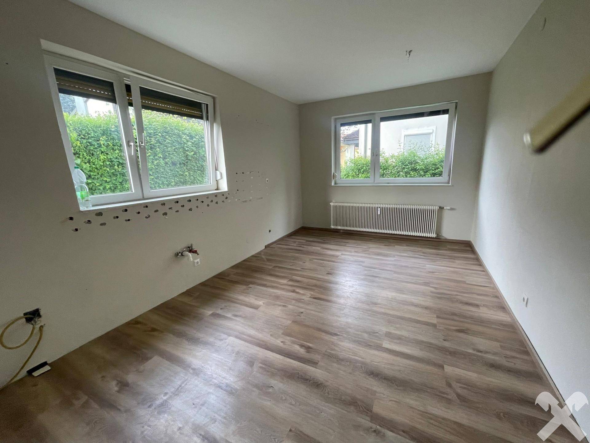 Leeres Zimmer mit Laminatboden, Fenster mit Rollladen und vorbereiteten Anschlüssen.