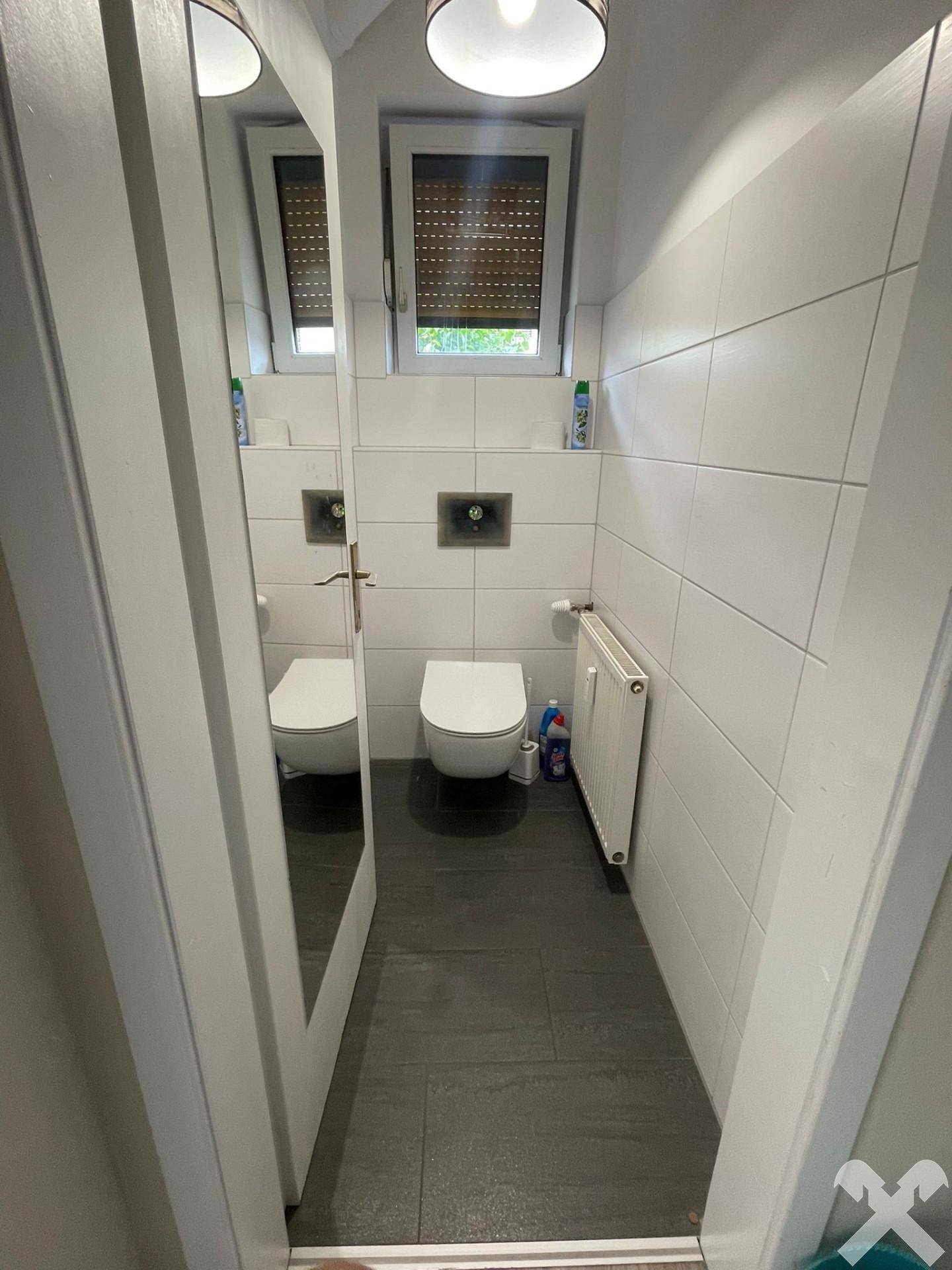 Modernes WC mit wandhängender Toilette, kleinem Waschbecken und weißen Fliesen.