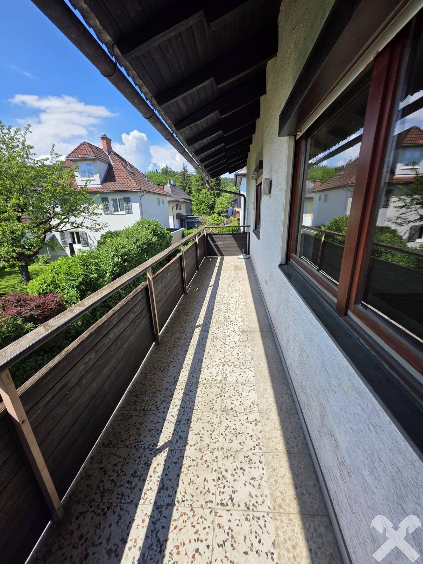 Langer, schmaler Balkon mit Fliesenboden und Holzgeländer, bietet Blick ins Grüne.