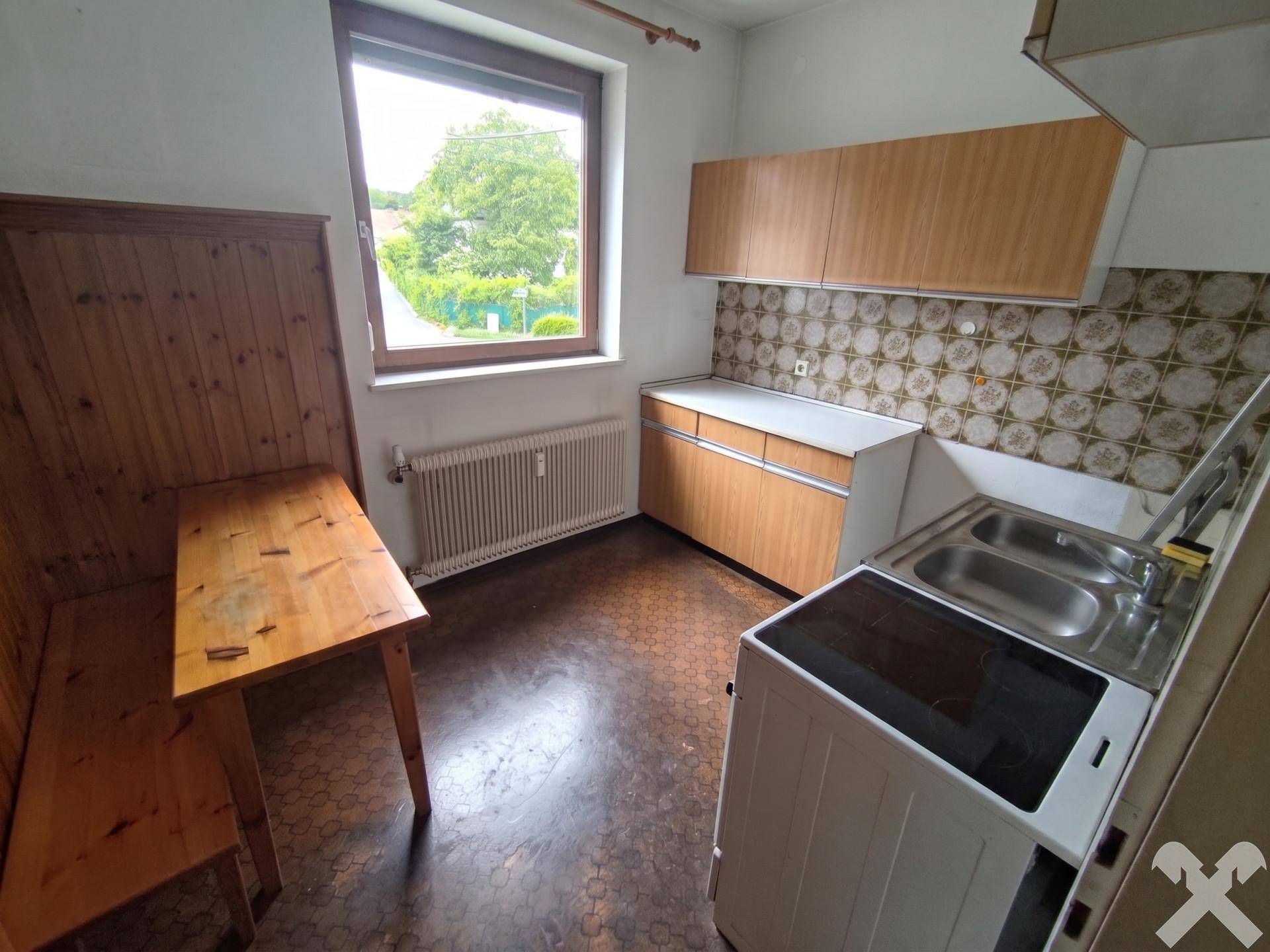 Einfache Küche mit Holzeckbank, Spüle und älteren Küchenschränken.