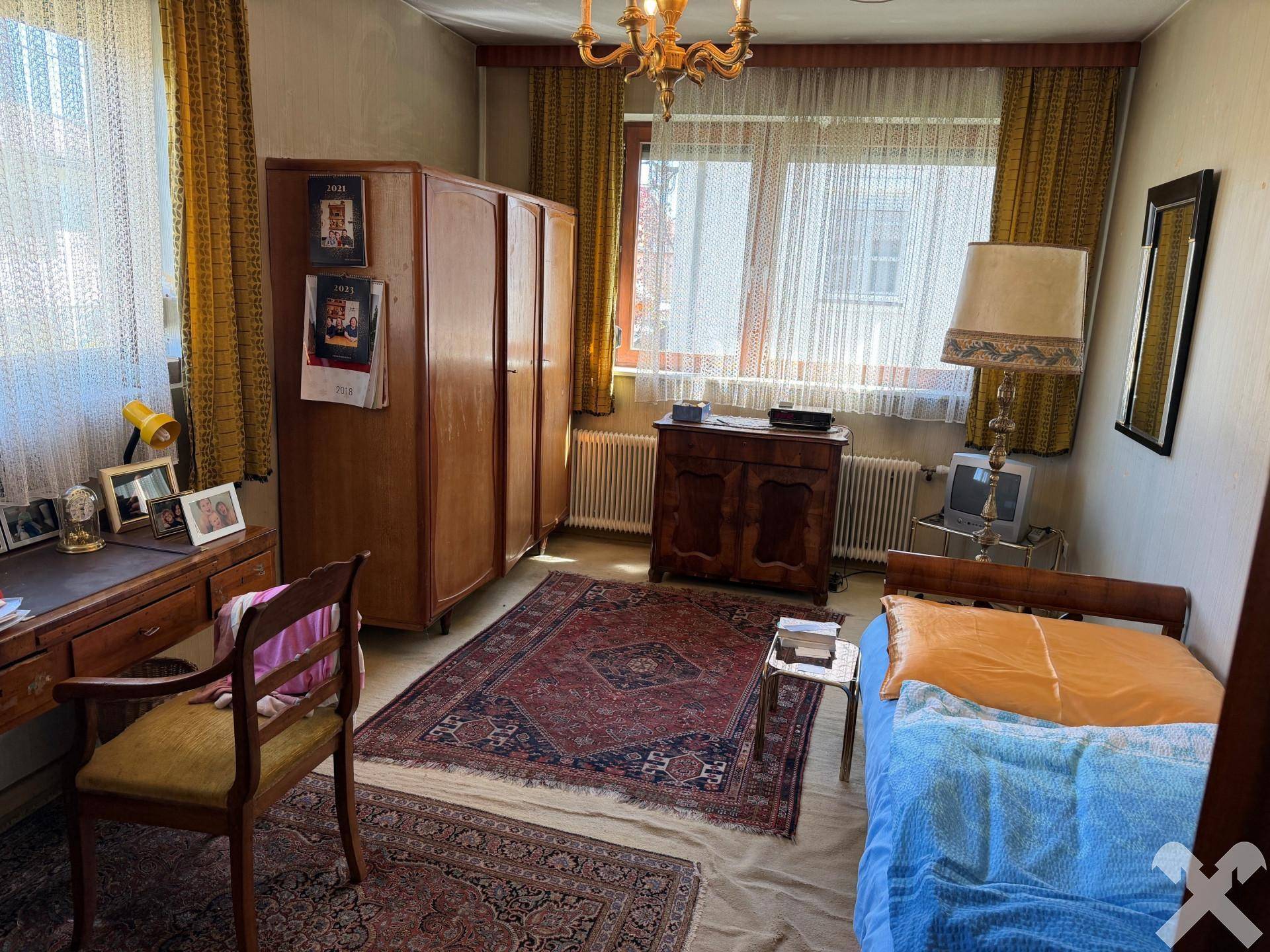 Schlafzimmer im traditionellen Stil mit Holzmöbeln, Teppich und großem Fenster.