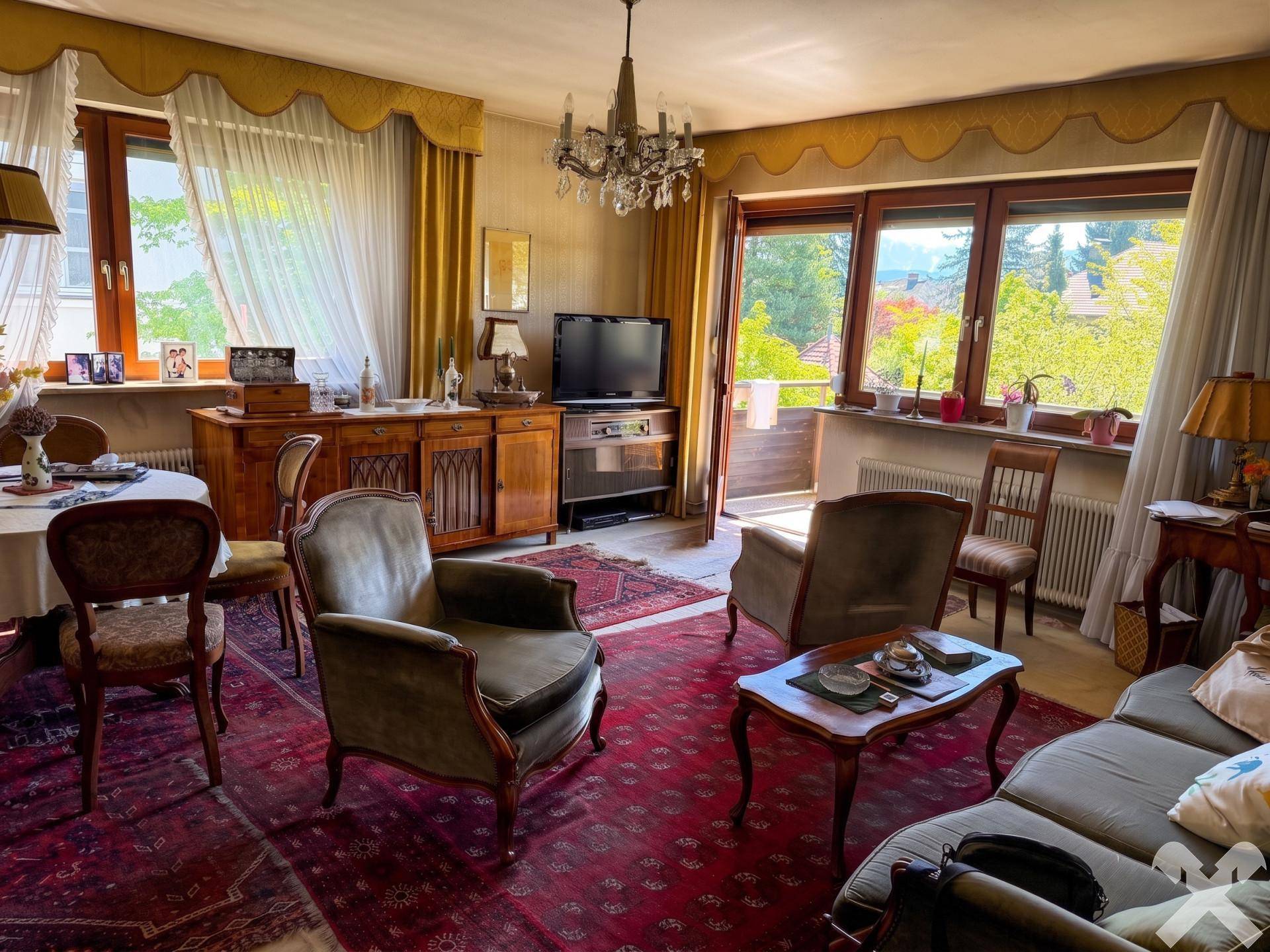 Gemütliches Wohnzimmer mit traditionellen Möbeln, Teppich und Zugang zum Balkon.