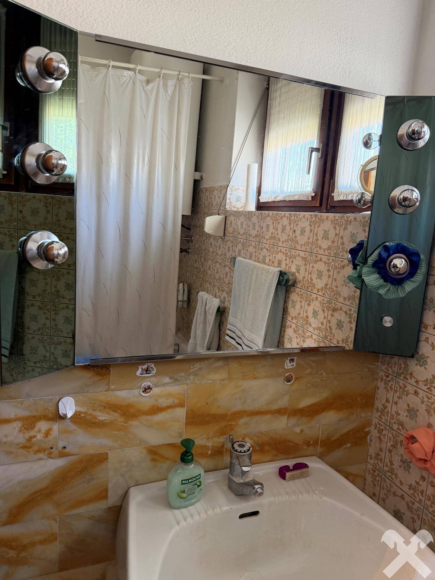 Badezimmer mit gelb-braunen Fliesen, Waschbecken und Spiegelflächen.
