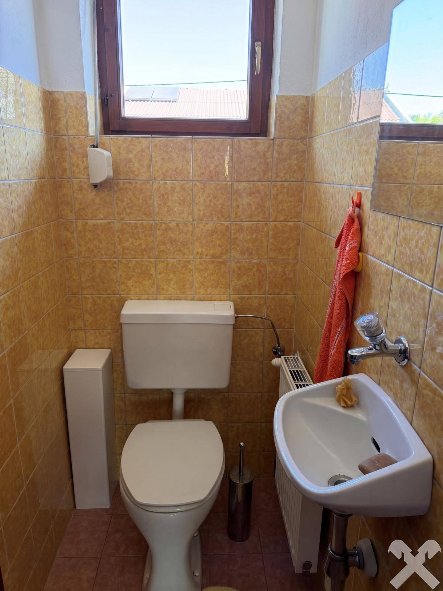 Kleines WC mit Toilette, Handwaschbecken und gelb-braunen Fliesen.