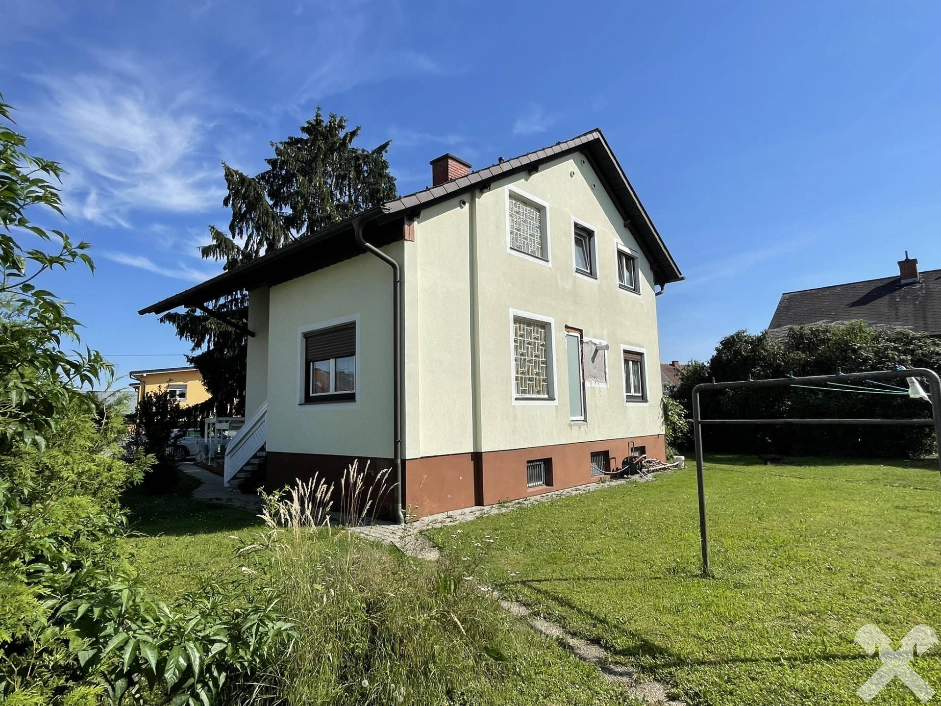 Rückansicht des Hauses mit hellgelber Fassade und braunem Sockel, umgeben von einem grünen Rasen.